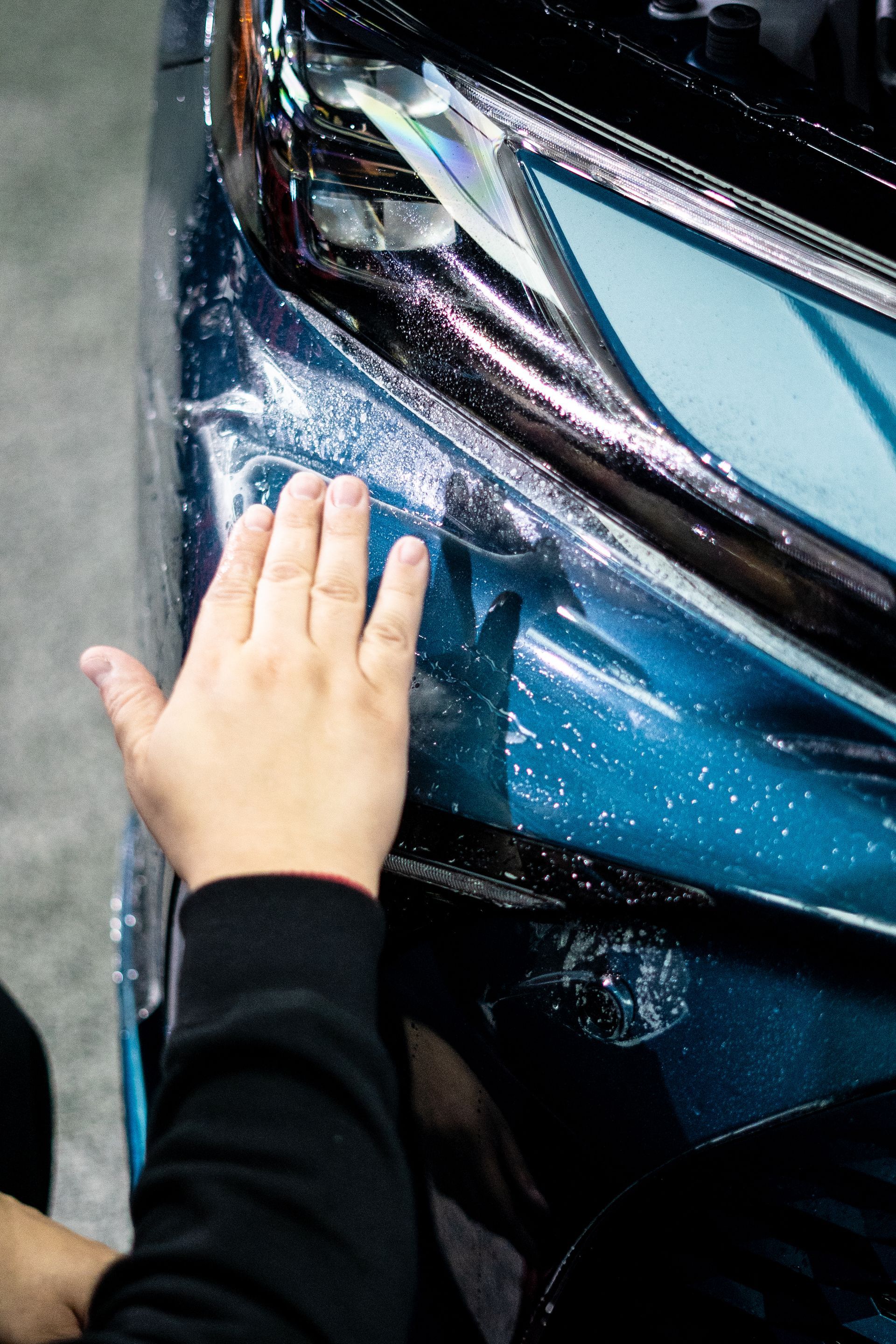 A person is touching the headlight of a car with their hand.