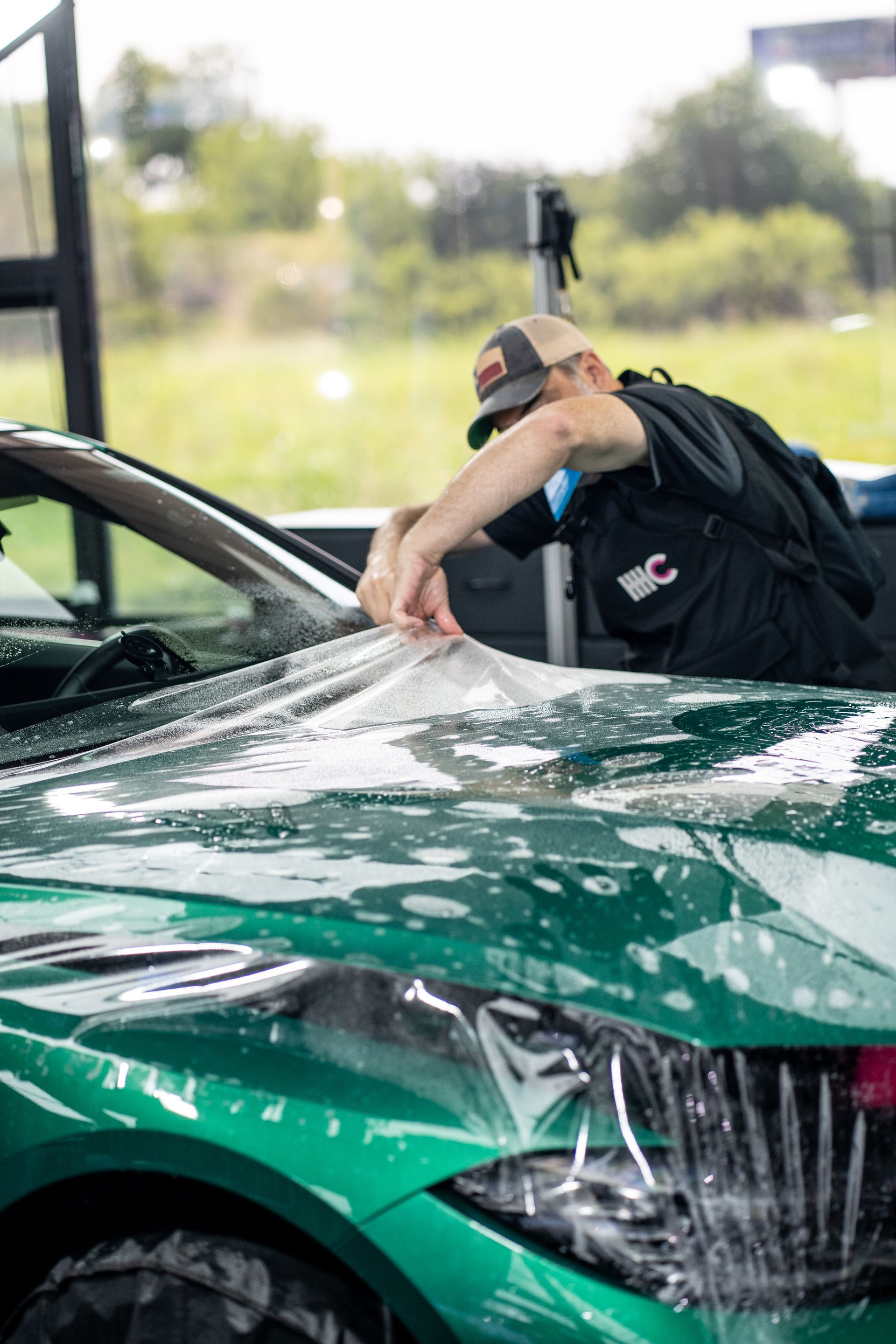 A man is wrapping a green car with plastic.