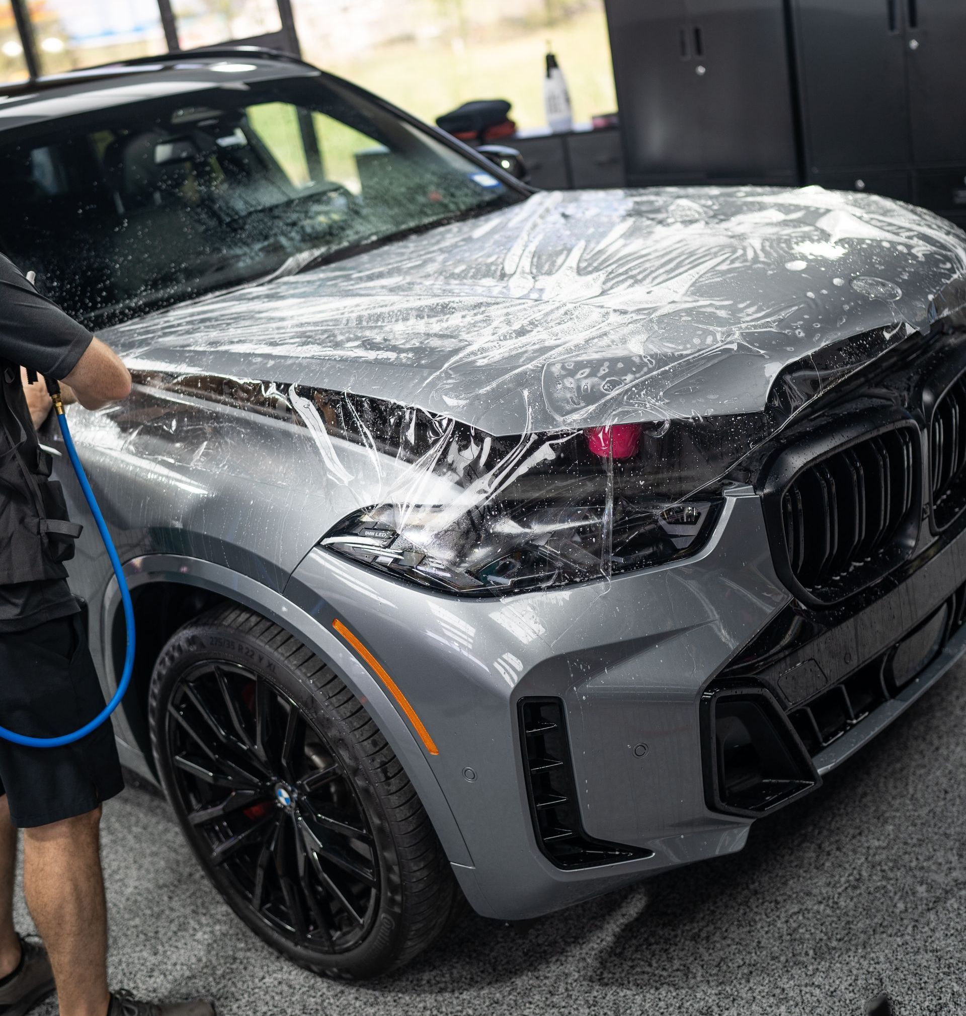 A man is cleaning a car with a hose in a garage.