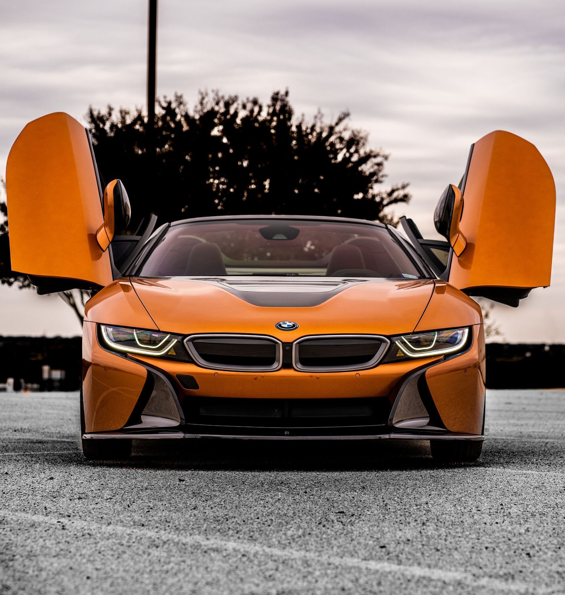 An orange sports car is parked in a parking lot with its doors open