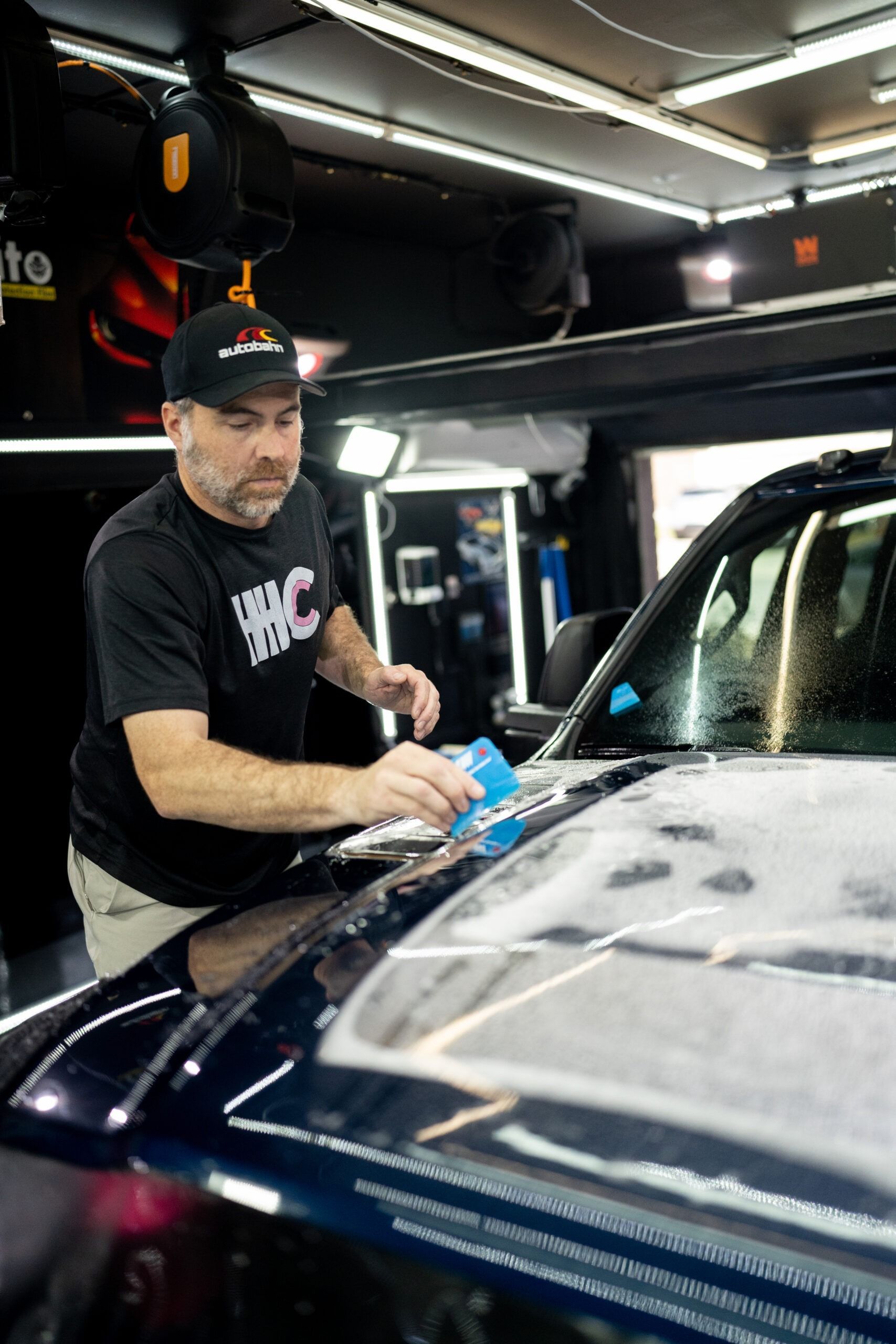 A man is cleaning the hood of a car in a garage.
