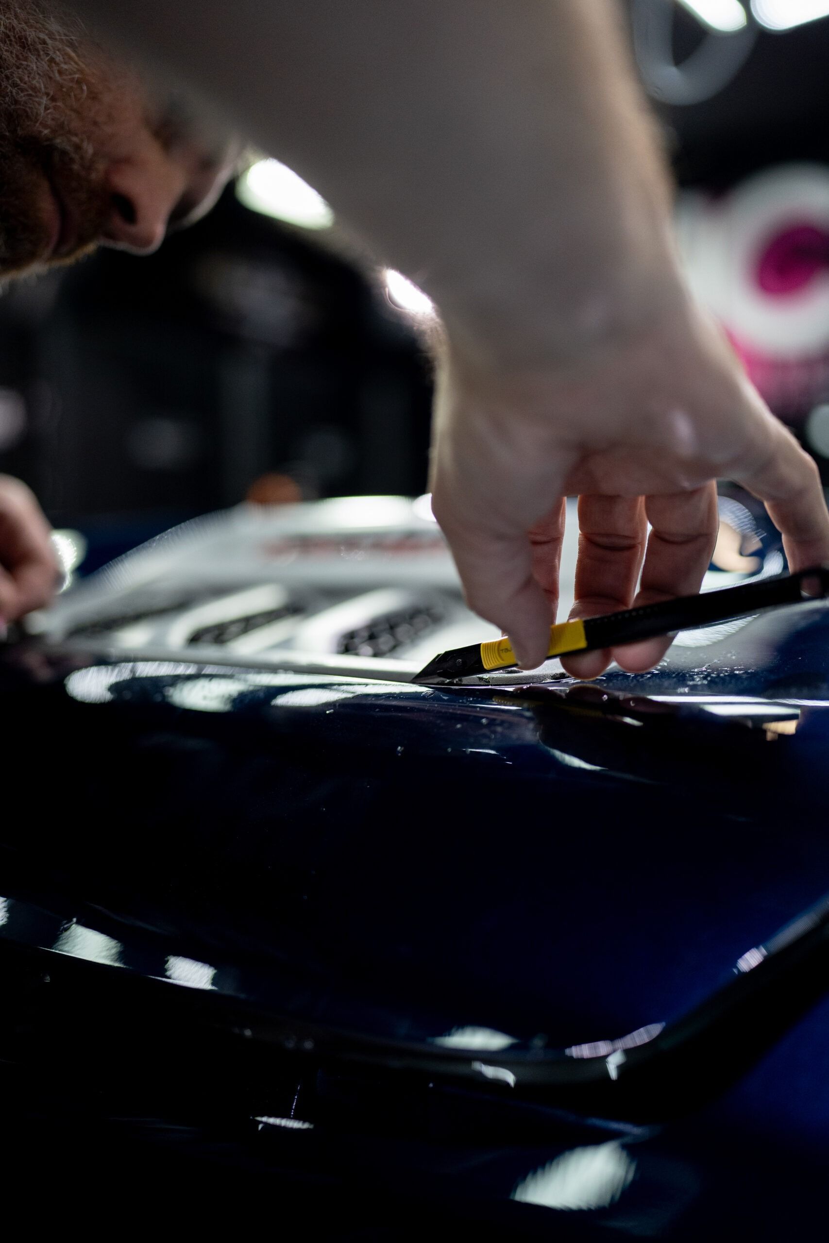 A man is working on a blue car with a screwdriver.