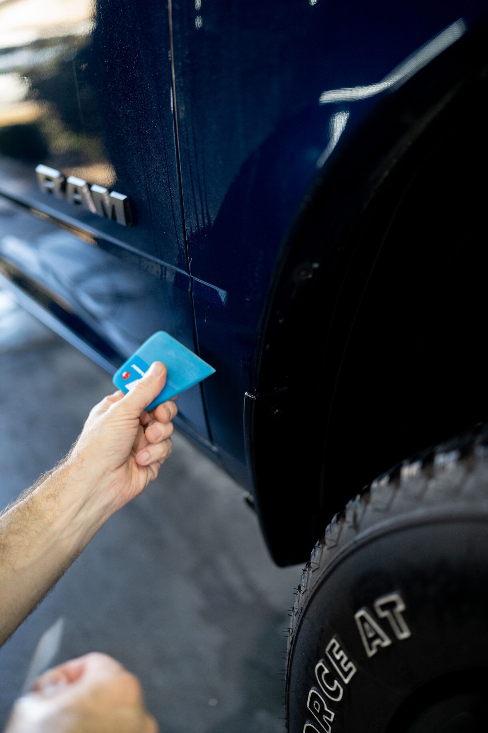 A person is cleaning the side of a blue ram truck.