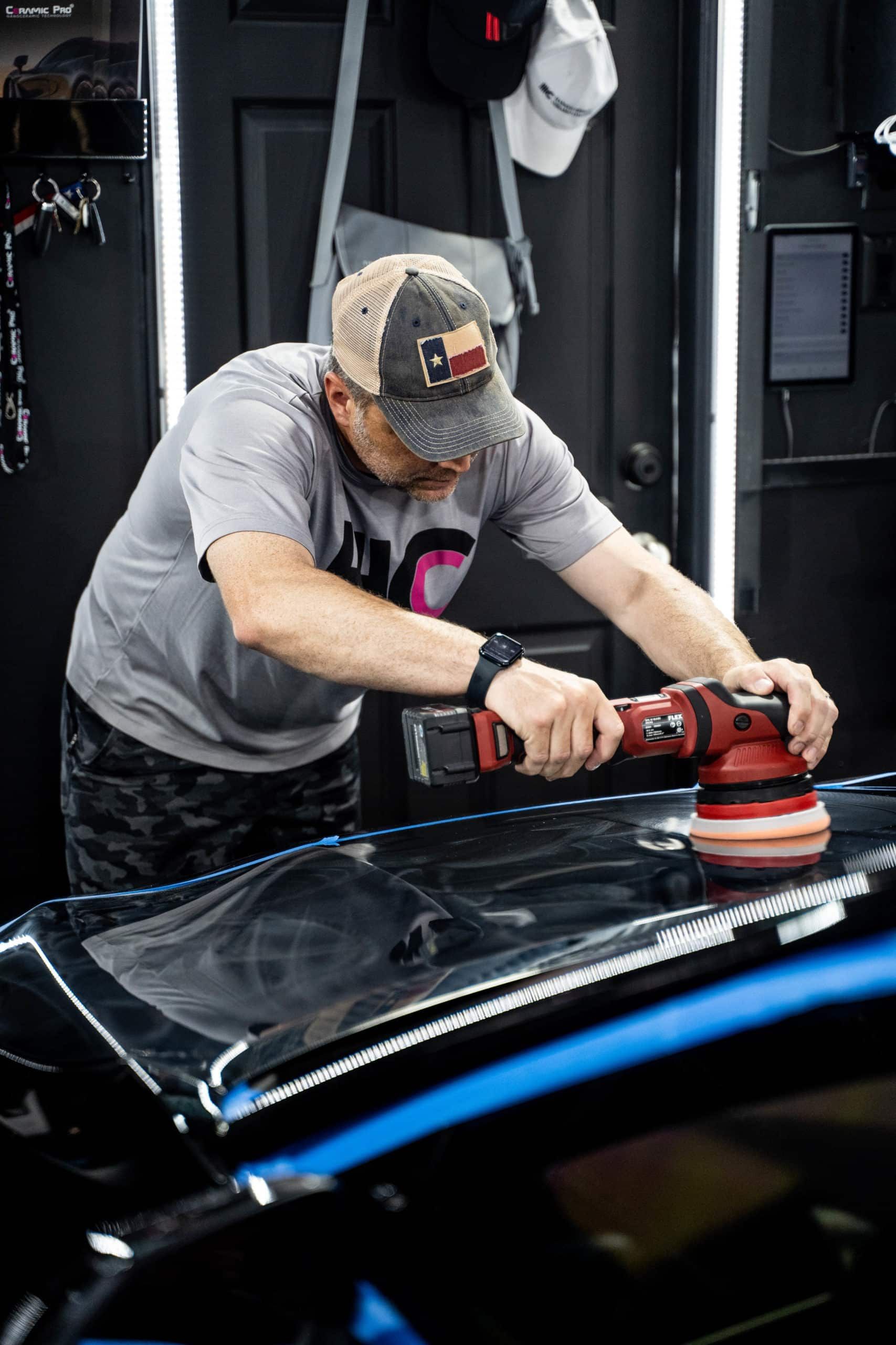 A man is polishing the hood of a car with a machine.