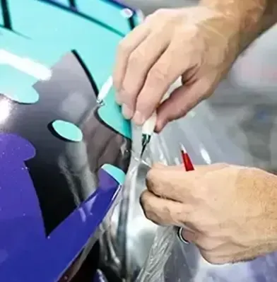 A man is wrapping a purple car with plastic wrap.