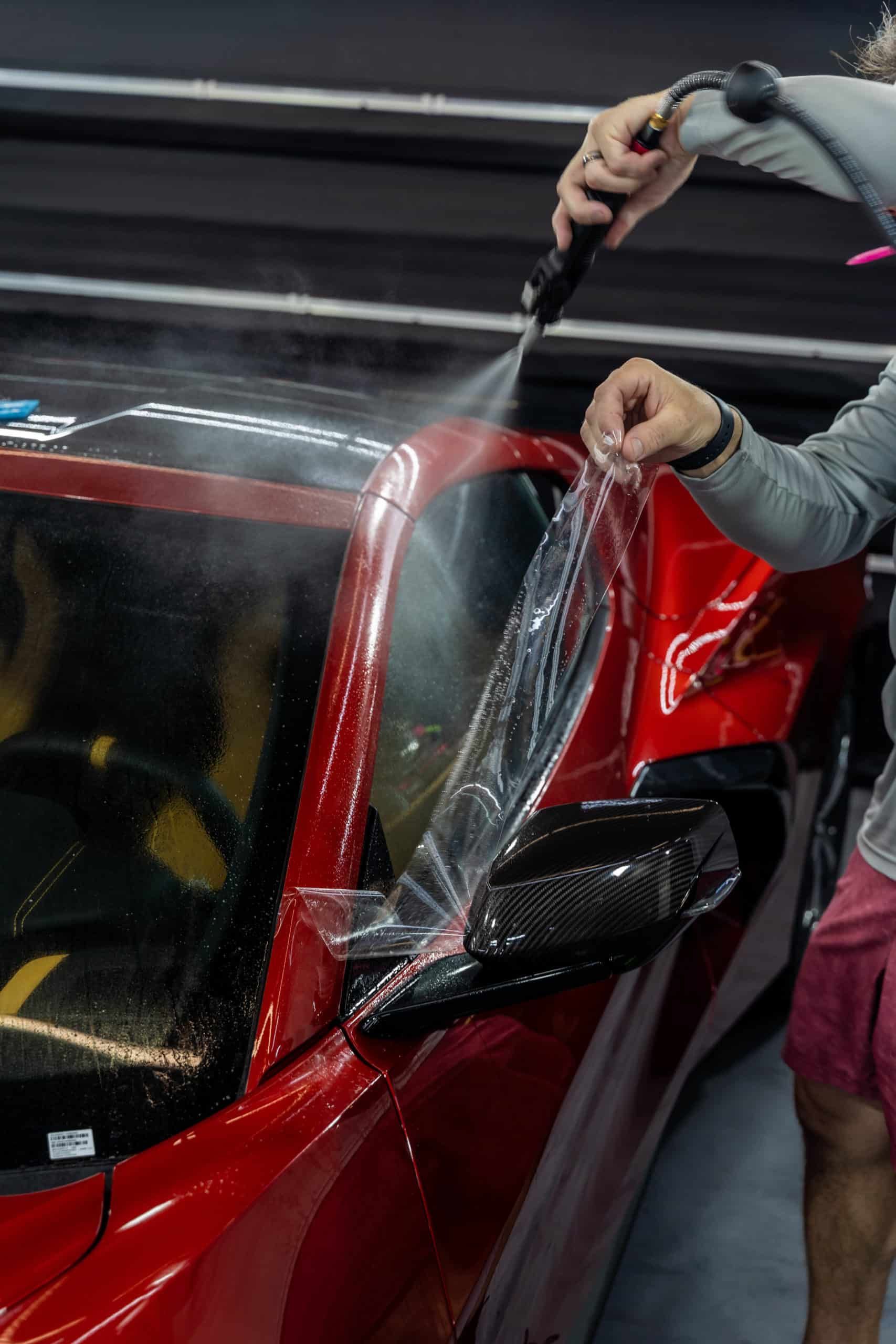 A man is spraying a red car with a spray bottle.