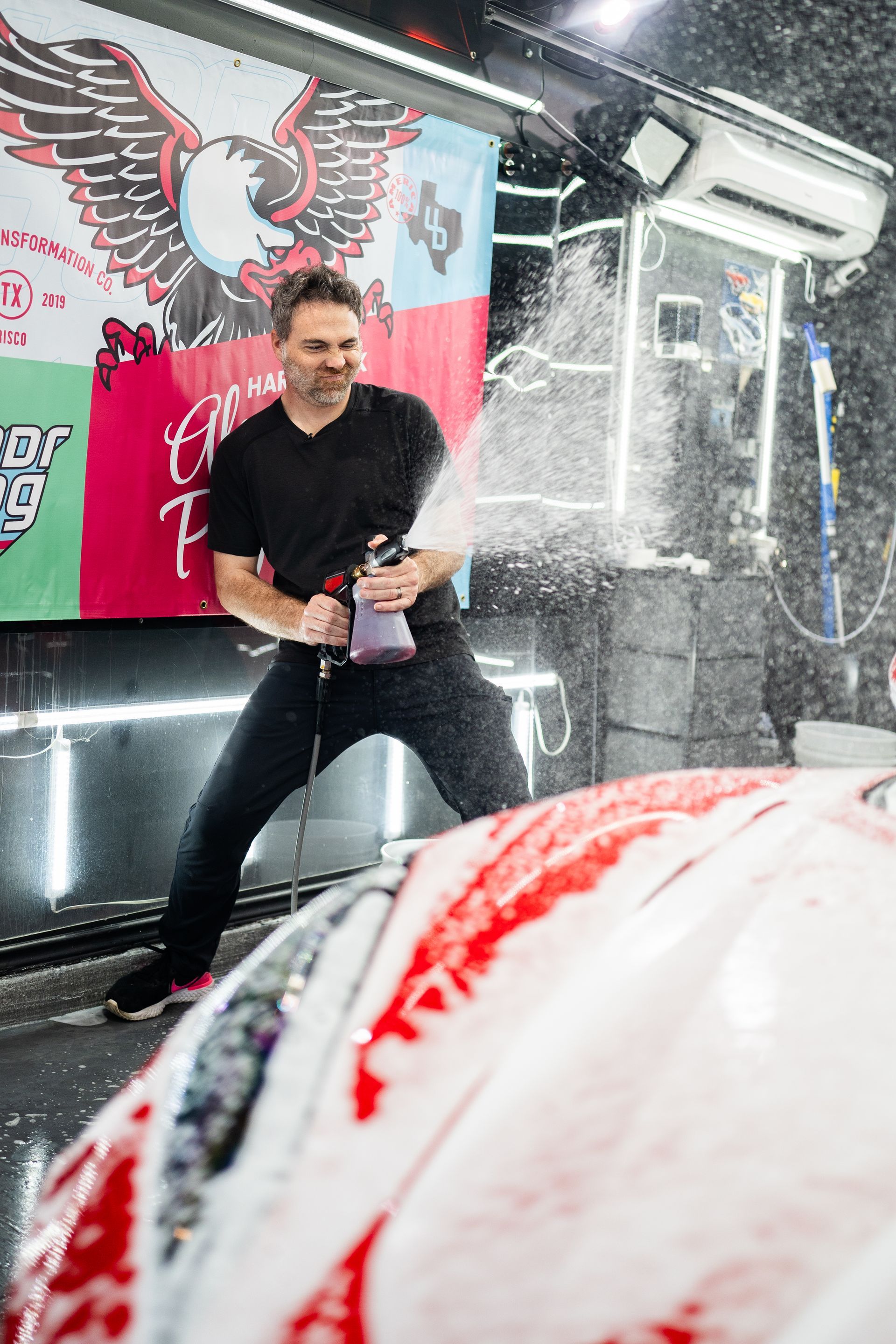 A man is spraying foam on a car in a car wash.
