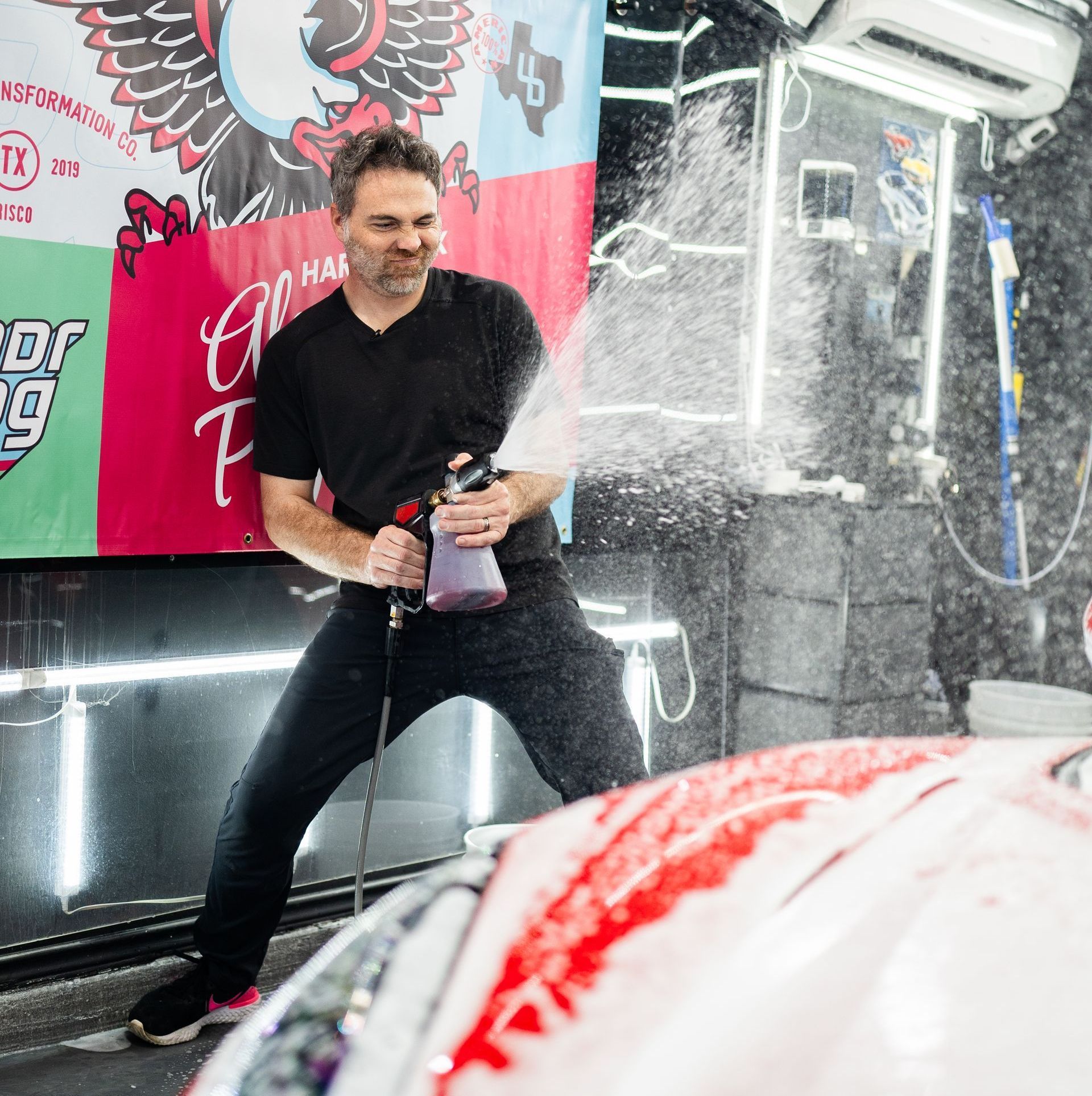 A man is spraying water on a car in a garage.