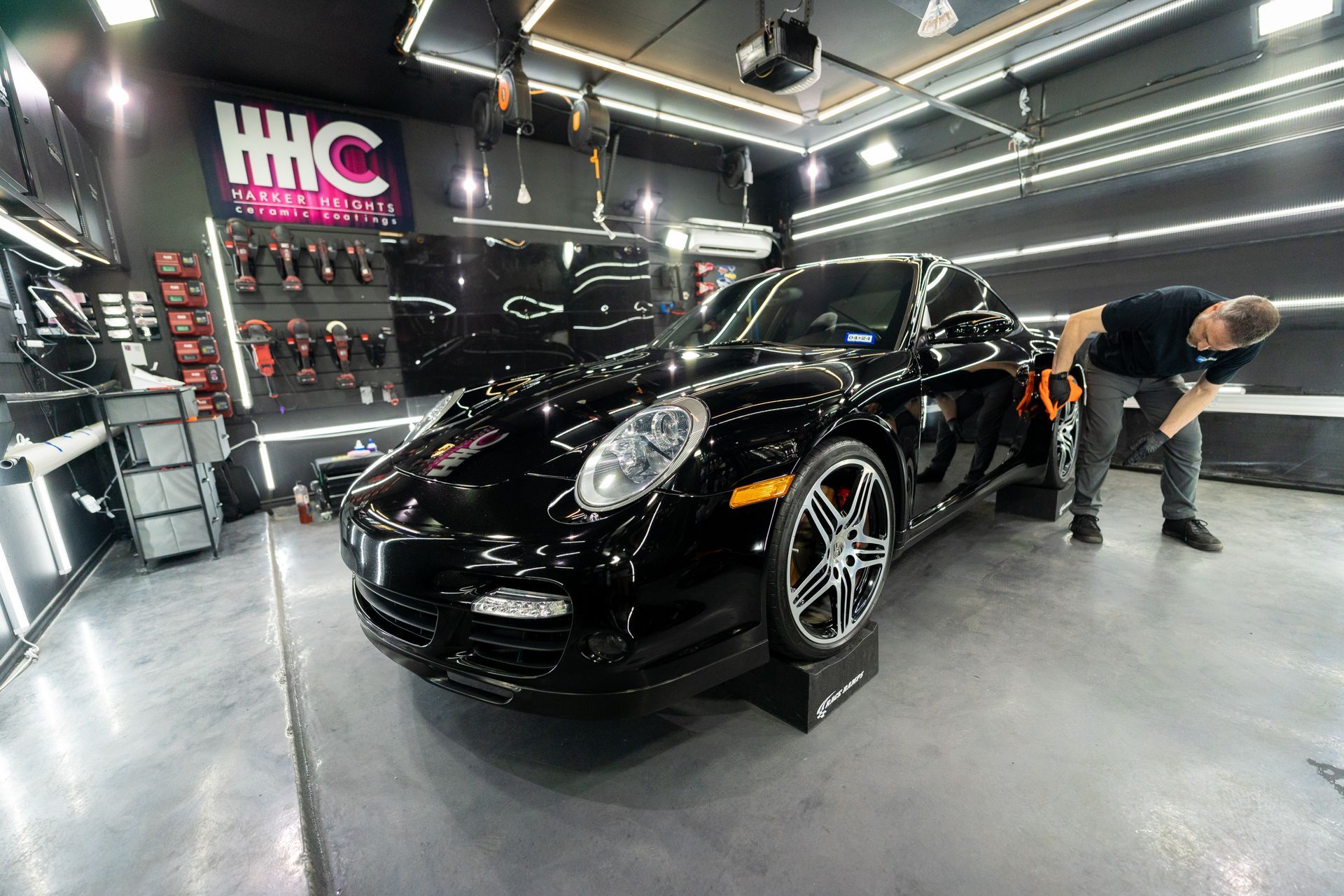 A man is cleaning a black car in a garage.