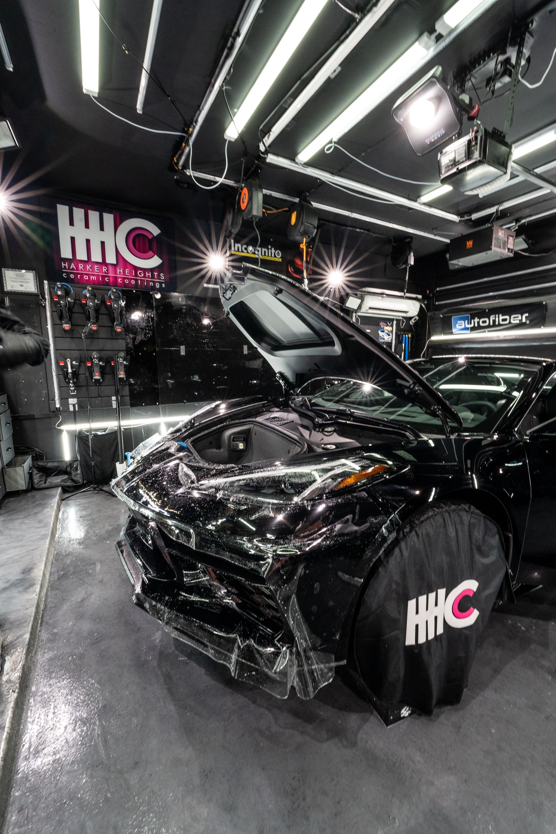 A black car is sitting in a garage with its hood up.