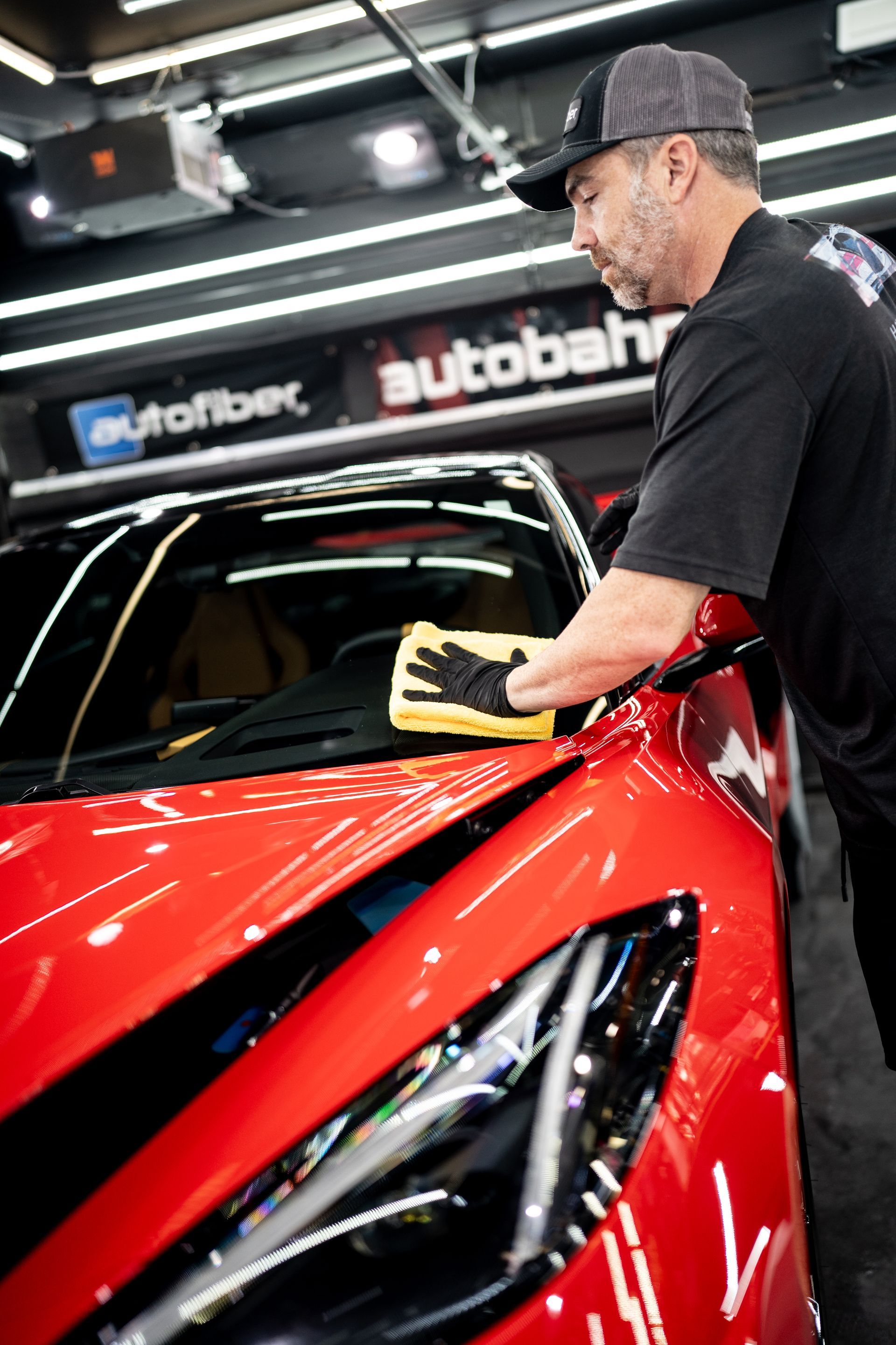 A man is cleaning a red sports car with a cloth.