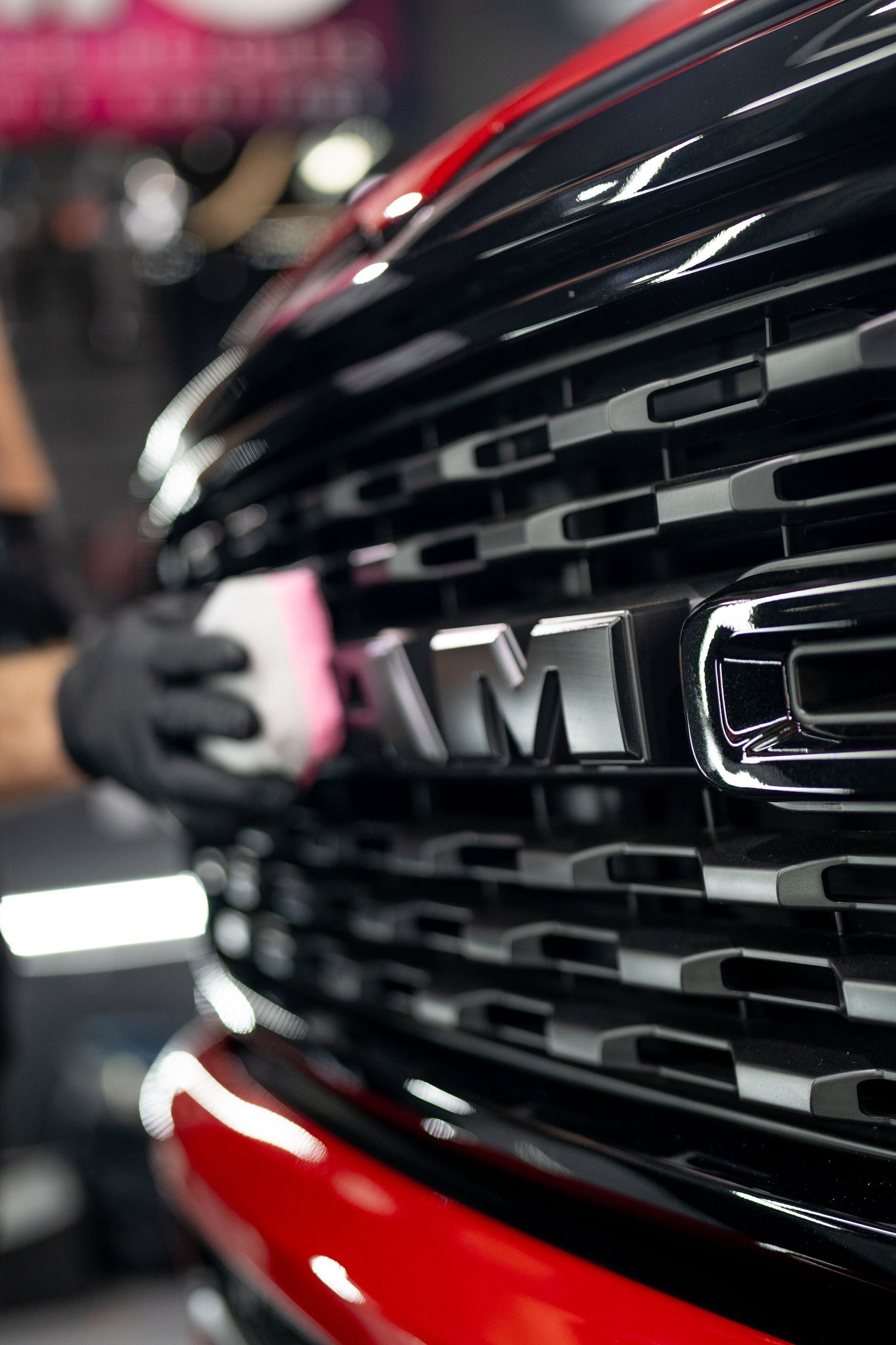 A person is cleaning the front grill of a red ram truck.