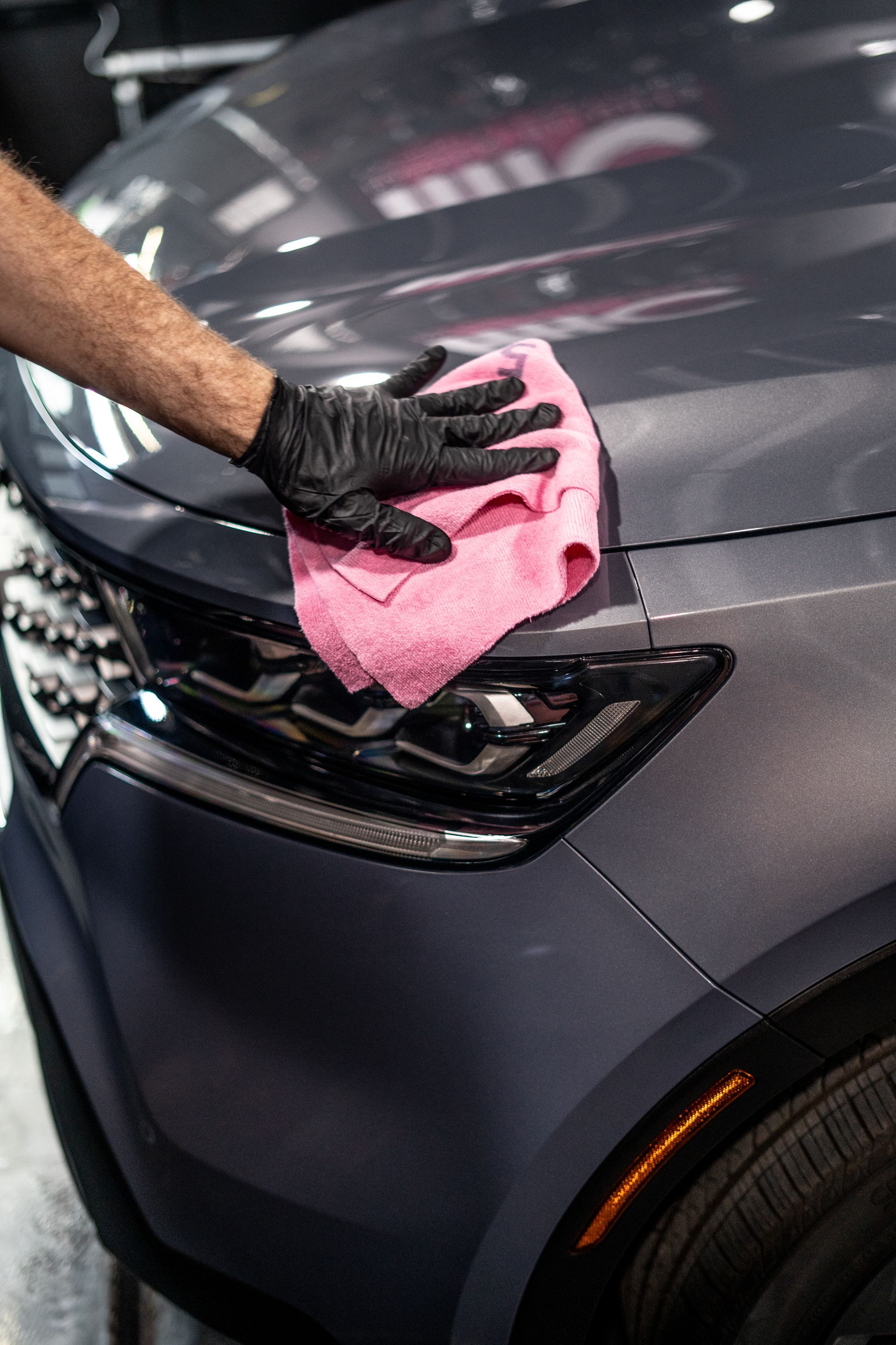 A person is cleaning a car with a pink cloth.