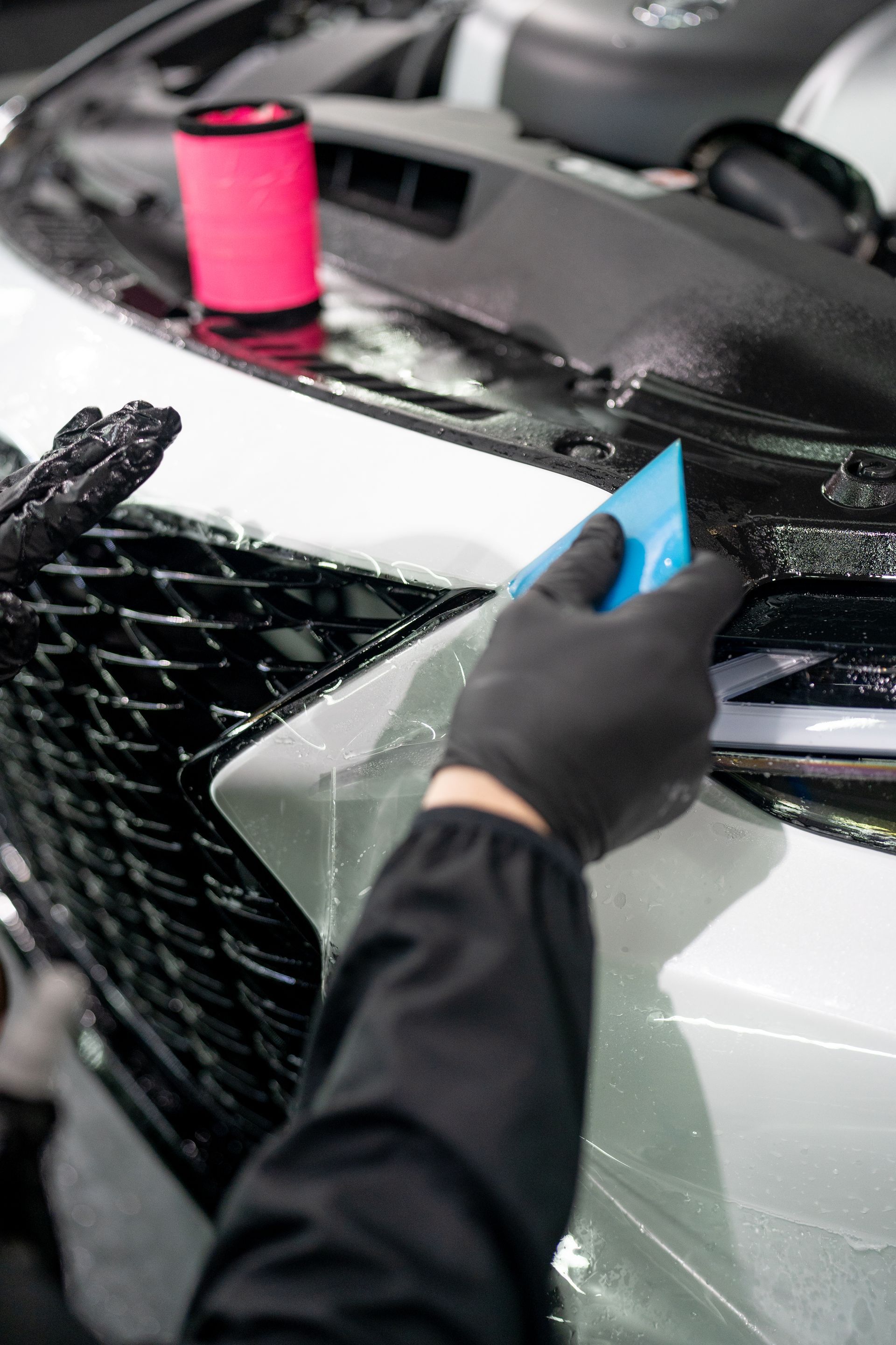 A person is applying a protective film to the front of a car.