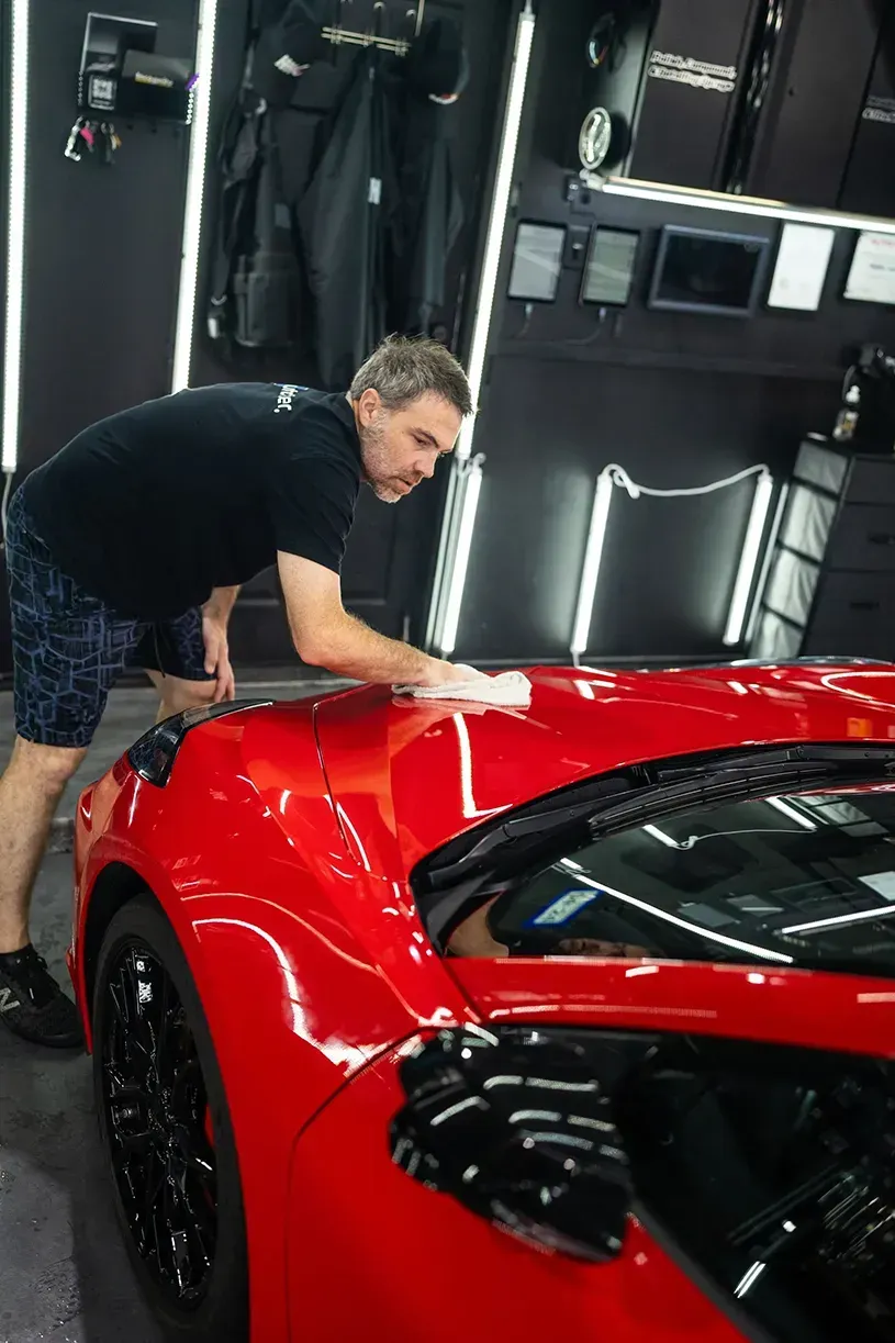 A man is cleaning a red sports car in a garage.