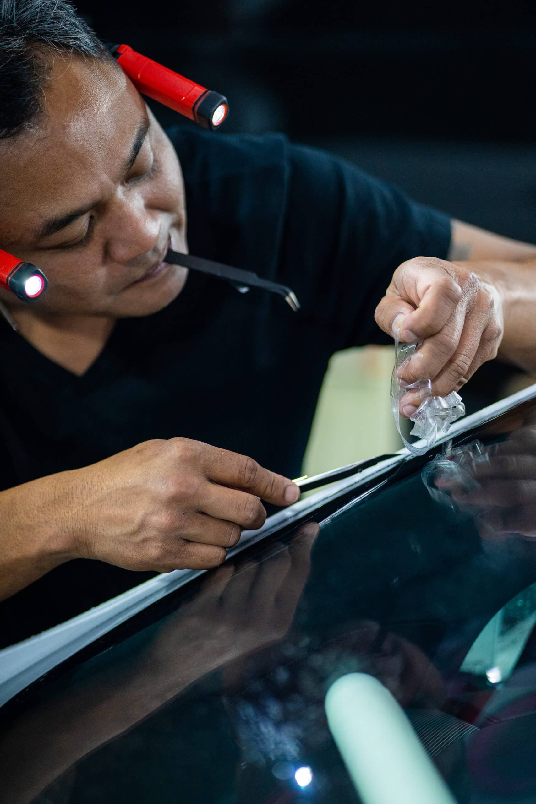 A man is working on a car windshield with a flashlight.