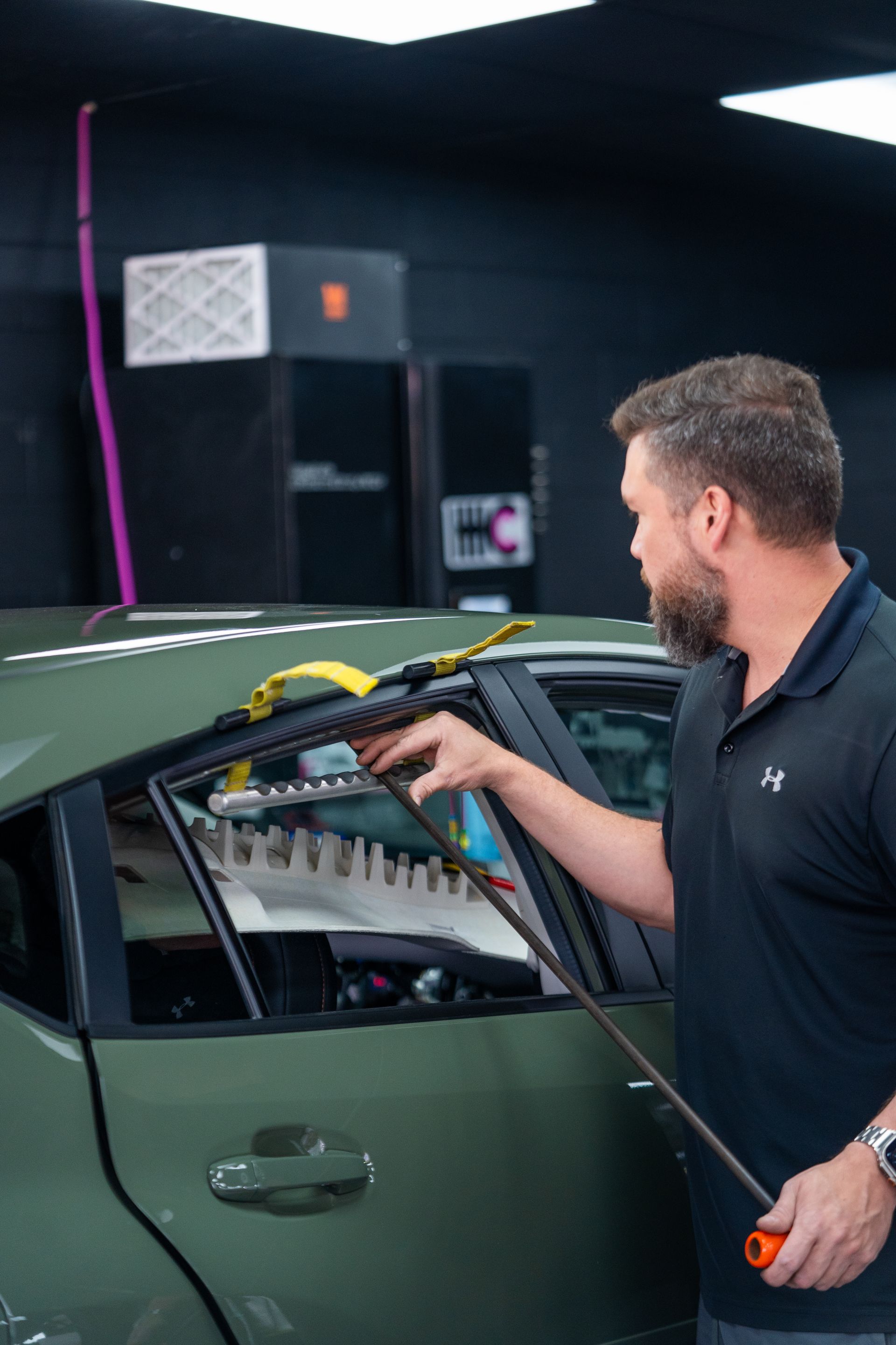 A man is working on a green car in a garage.