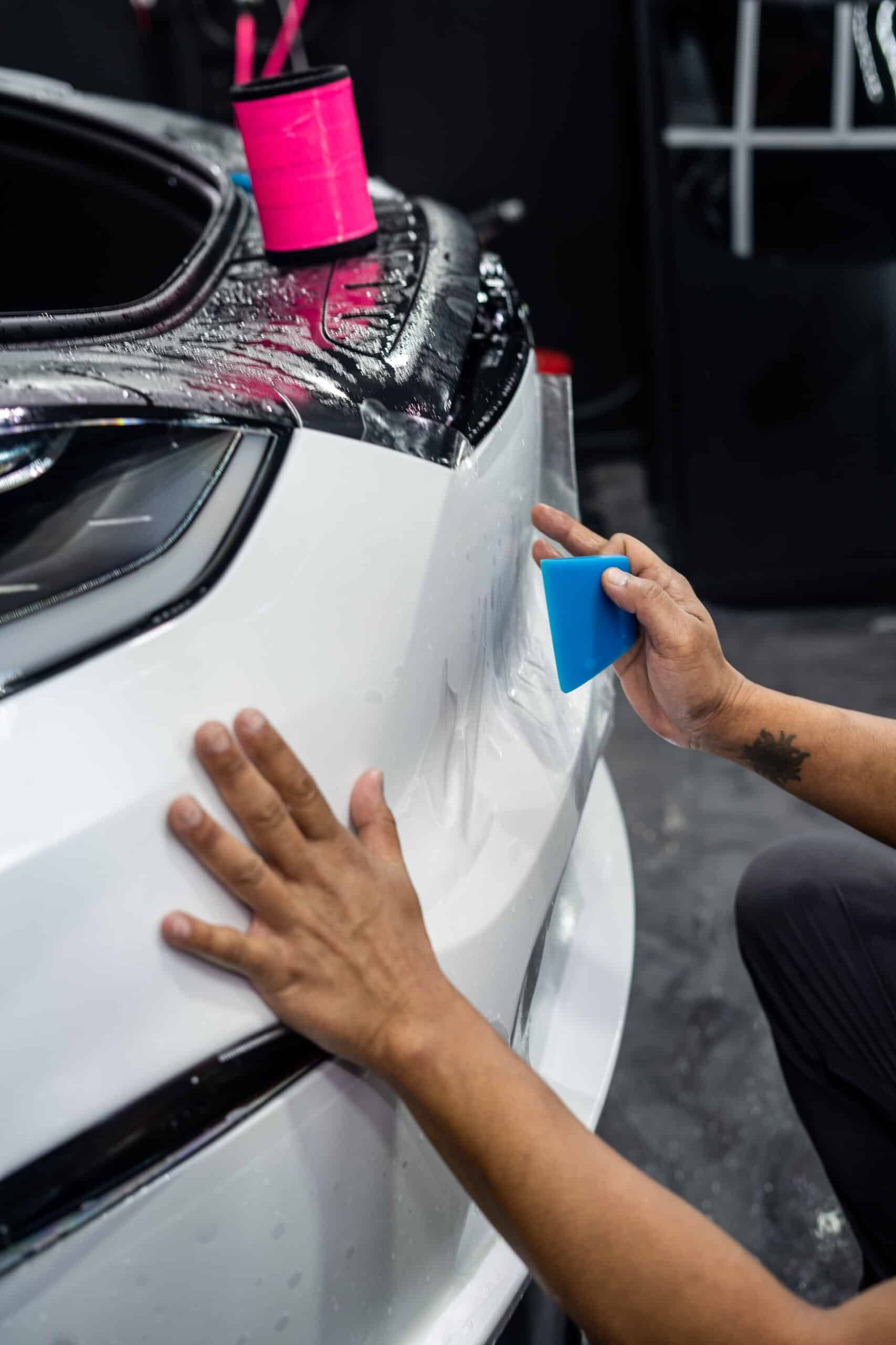 A person is applying protective film to a white car.