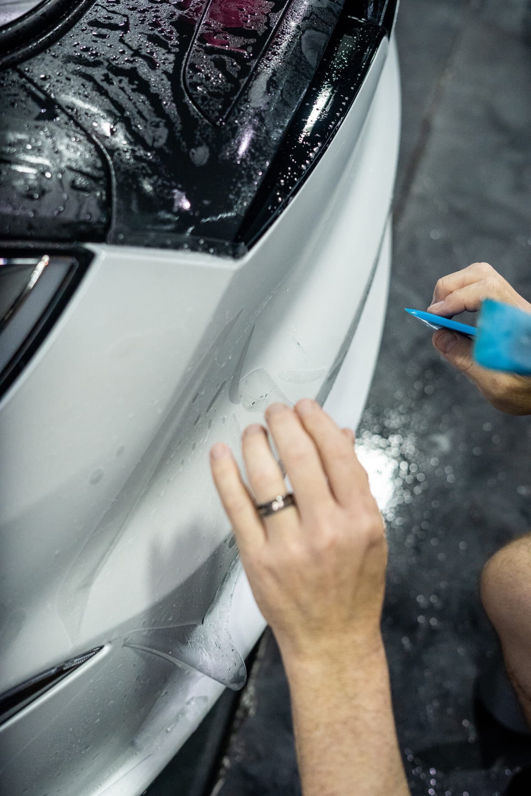 A person is applying a clear film to the front of a car.