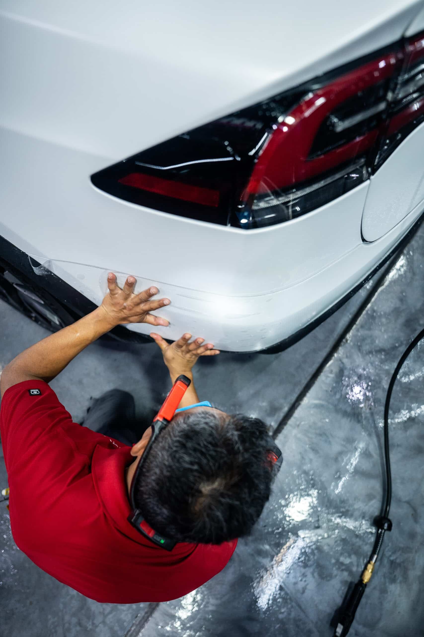 A man in a red shirt is working on the back of a white car.