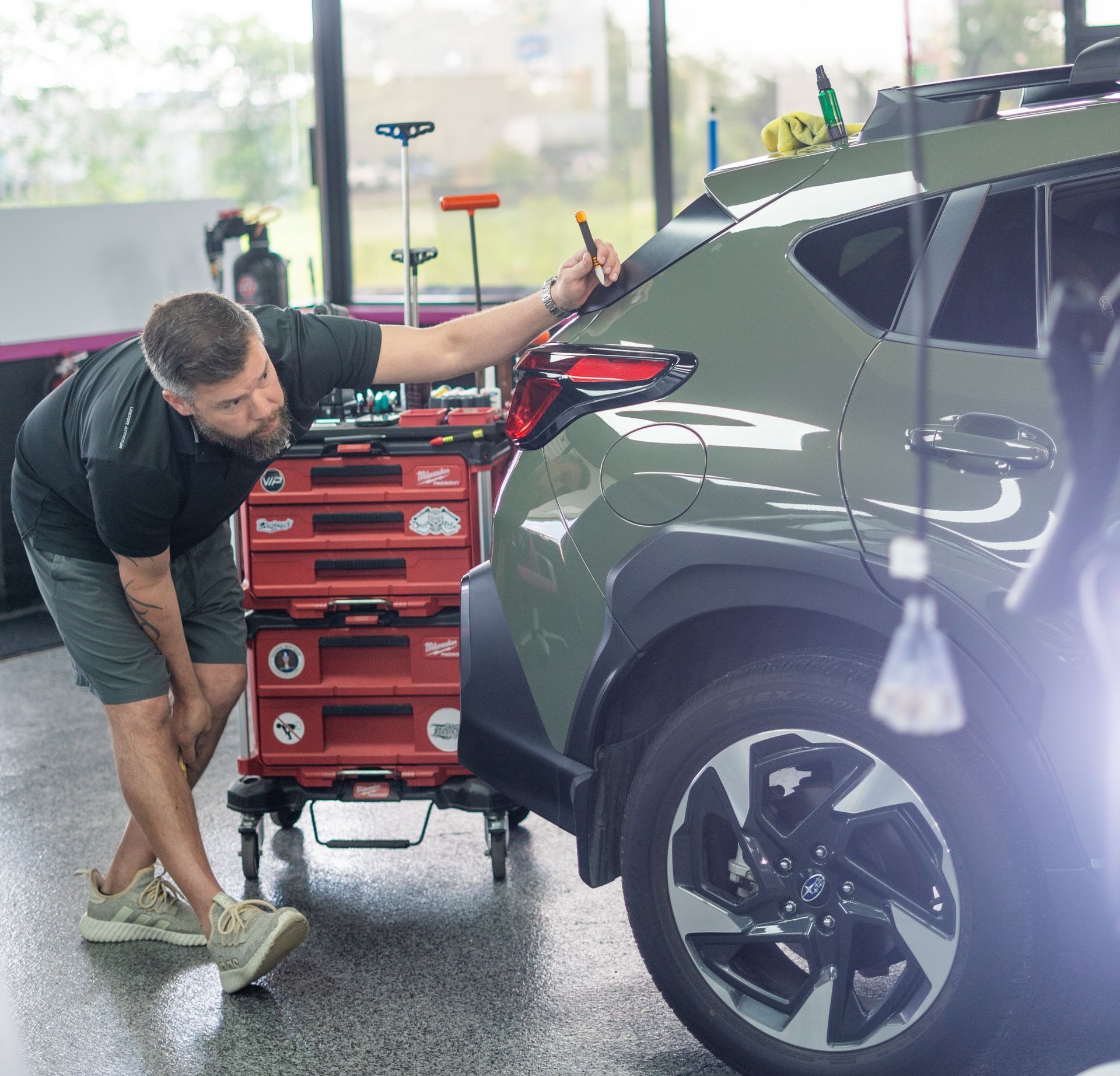 A man is cleaning a red sports car in a garage.