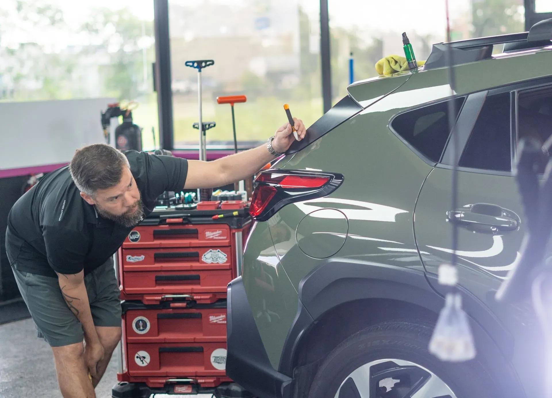 A man is polishing the hood of a red car.
