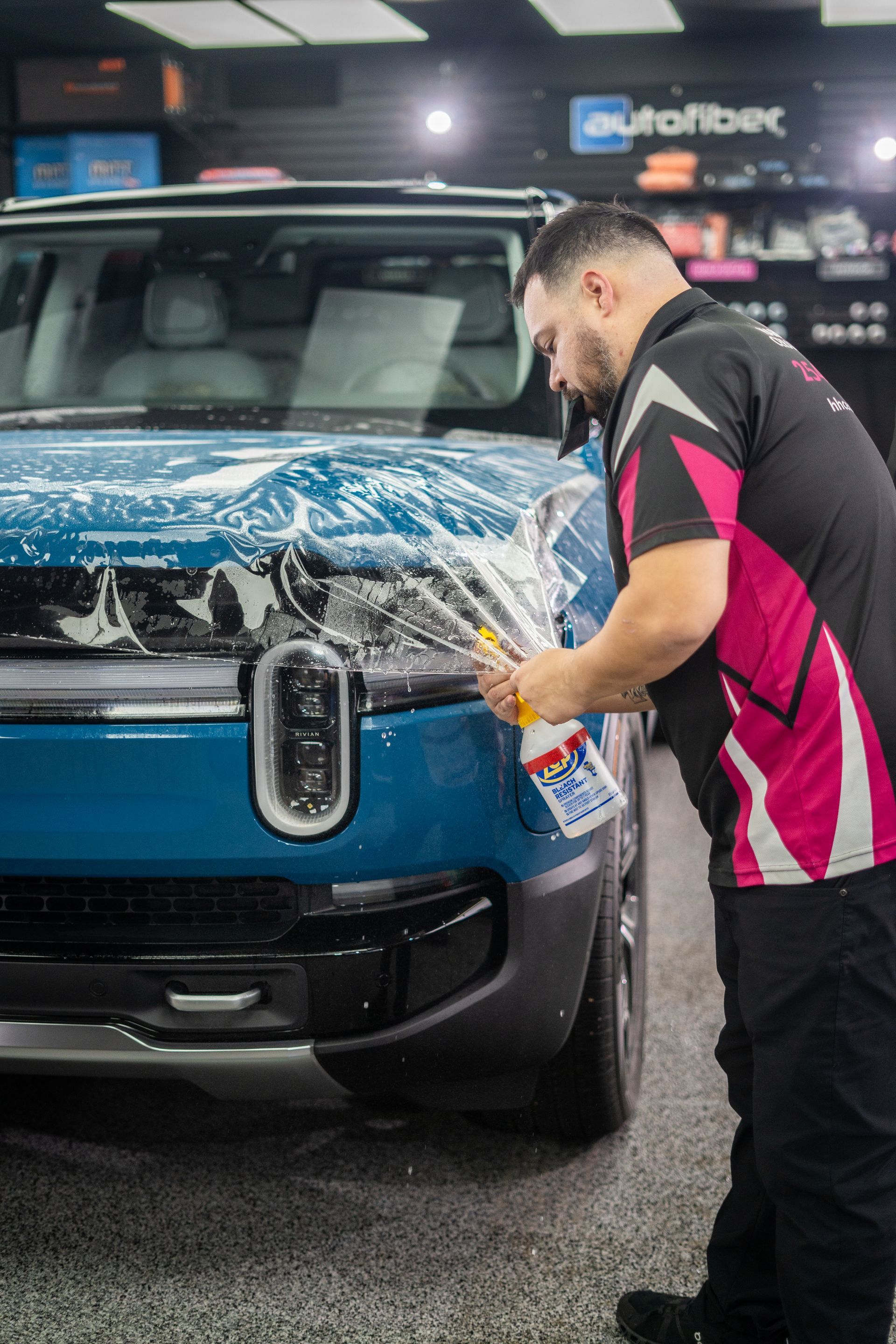A man is applying a protective film to the hood of a blue suv.