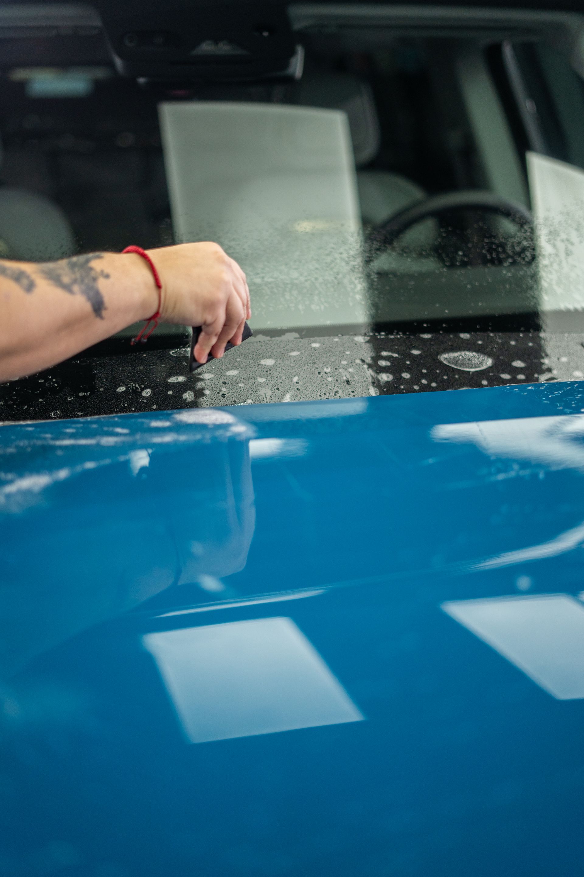 A woman is cleaning the windshield of a blue car.