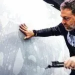 A man is cleaning the windshield of a car with a brush.