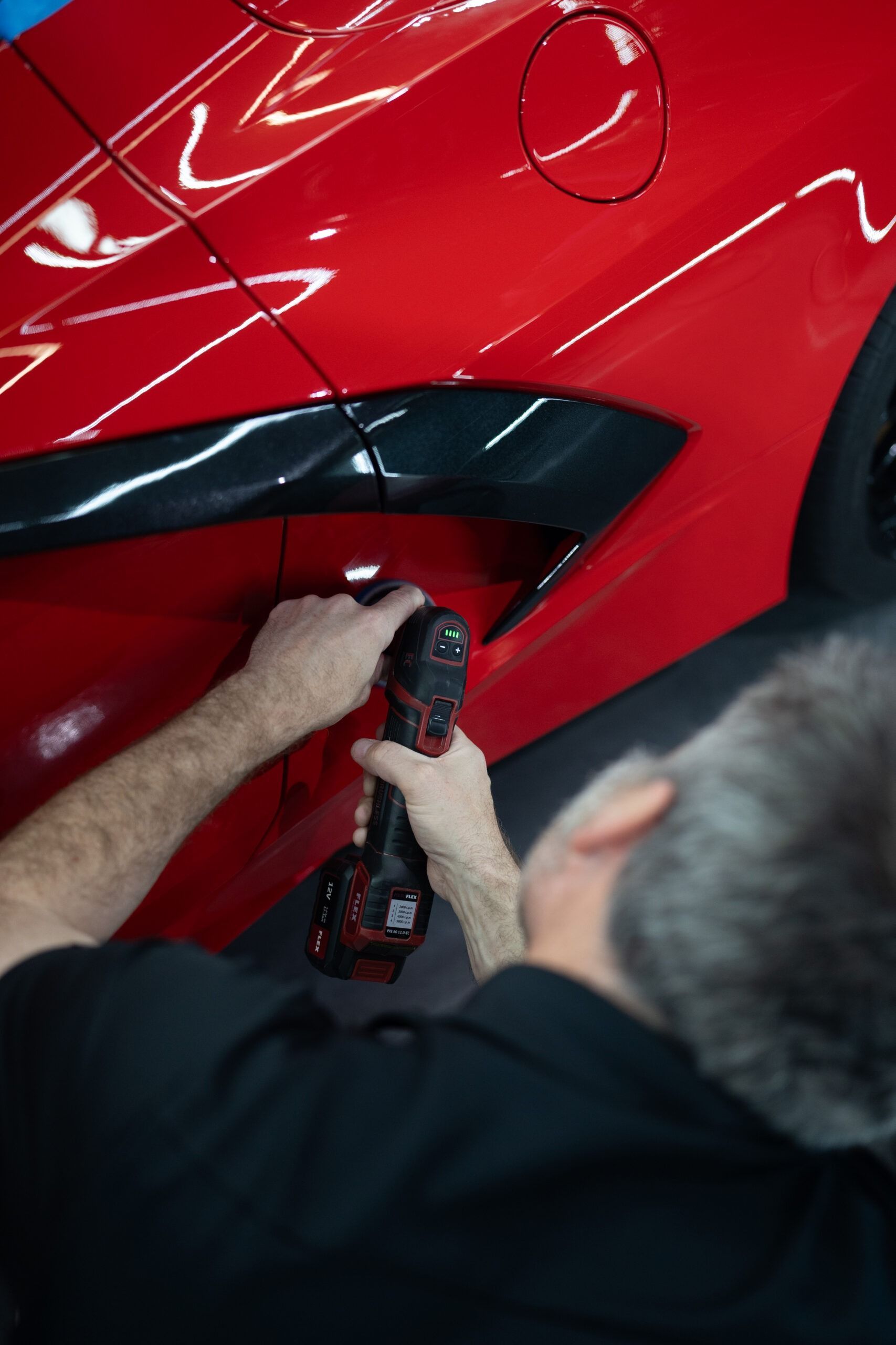 A man is working on a red car with a drill