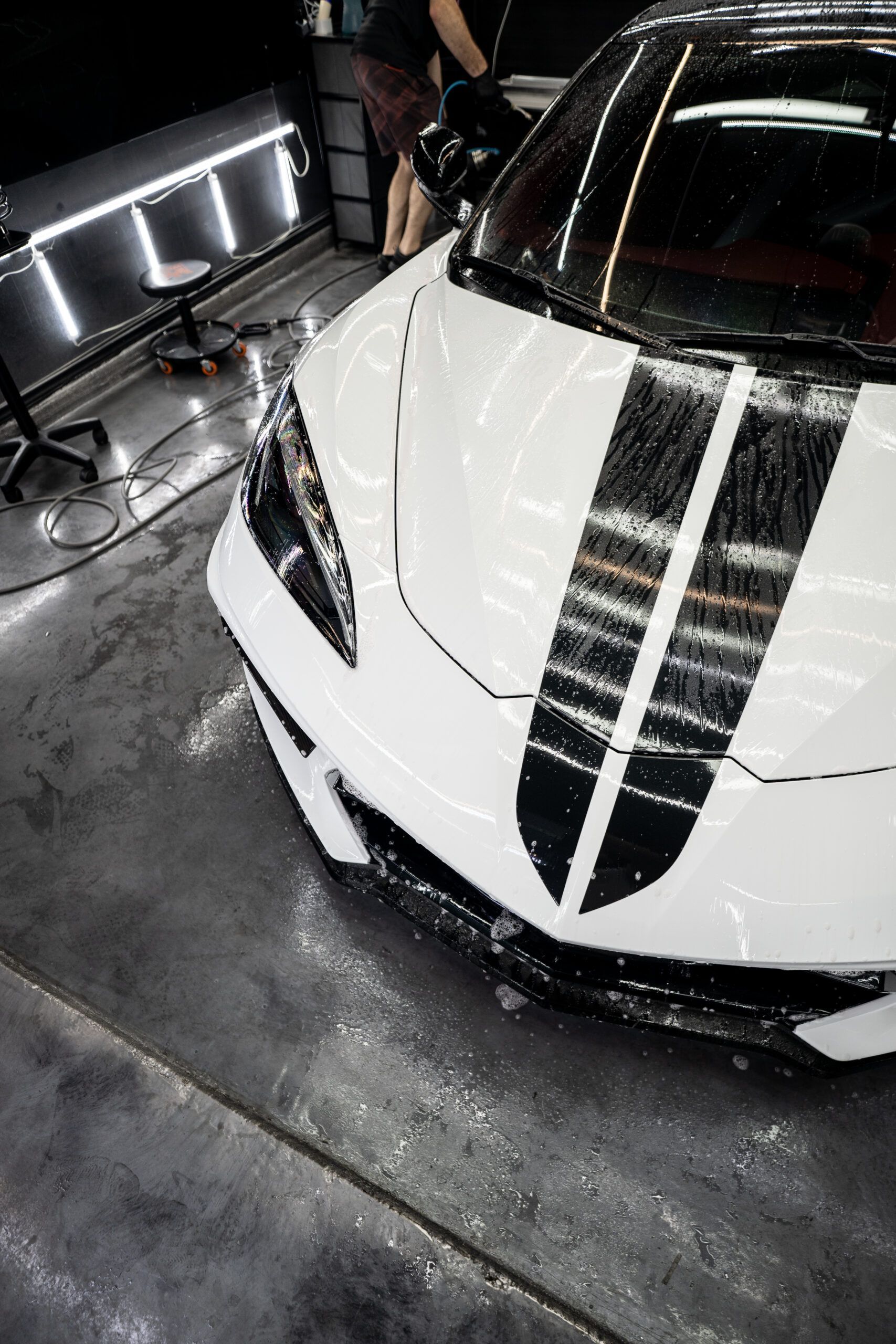 A white sports car with black stripes on the hood is being cleaned in a garage.