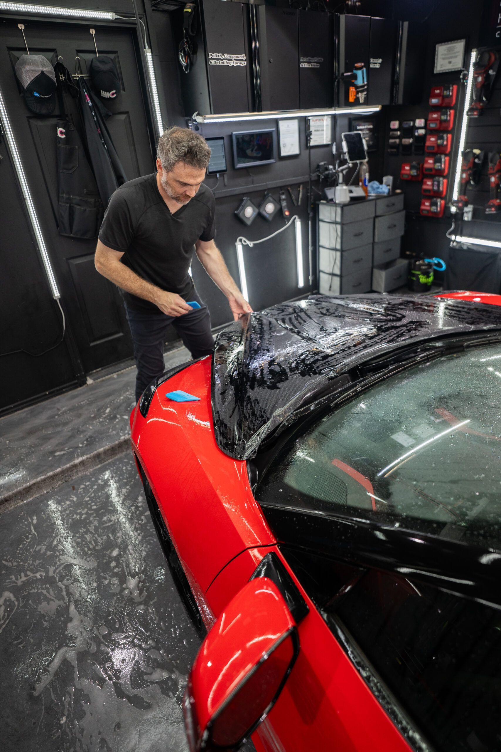 A man is washing a red sports car in a garage.