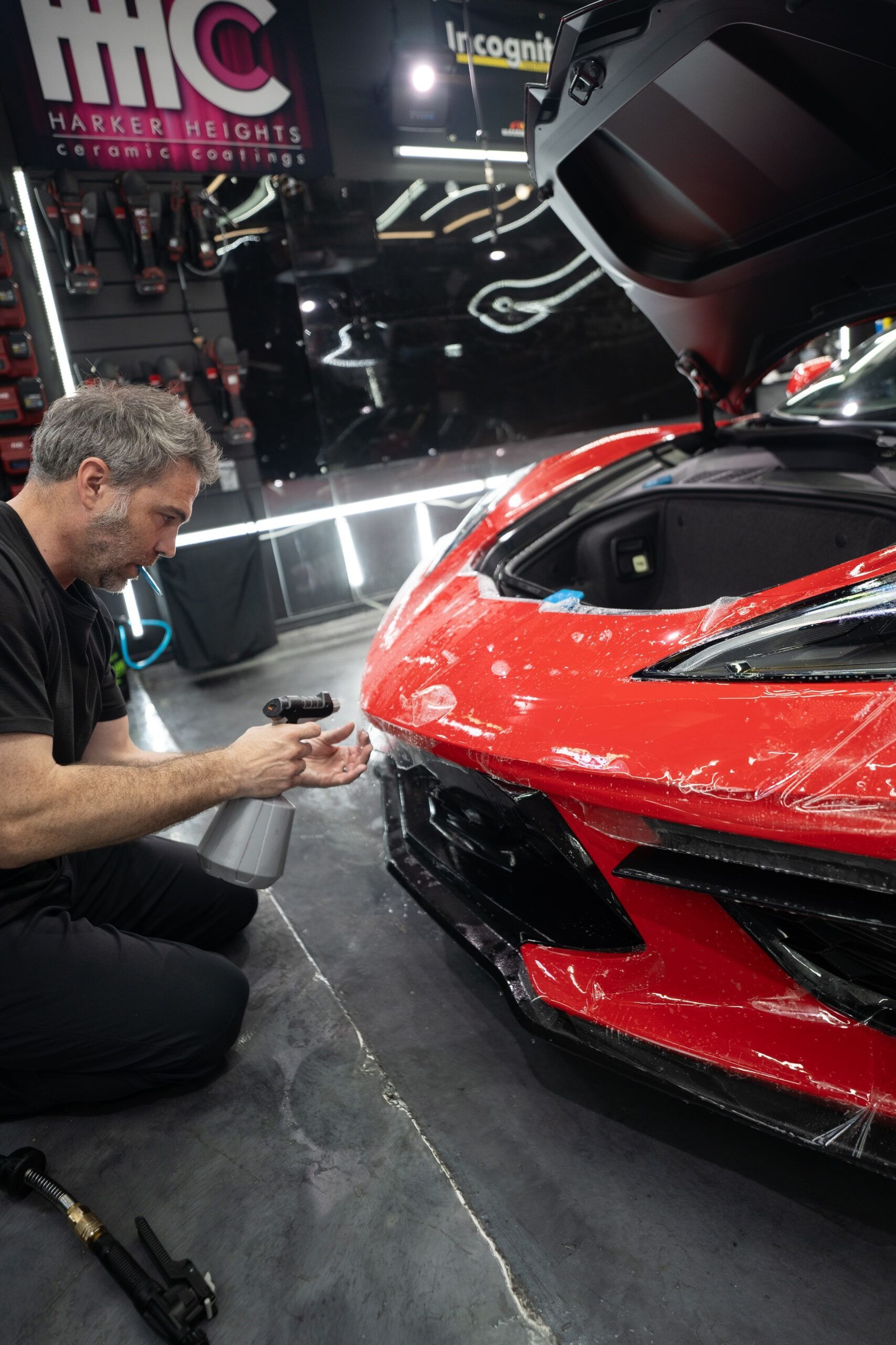 A man is kneeling down next to a red sports car.