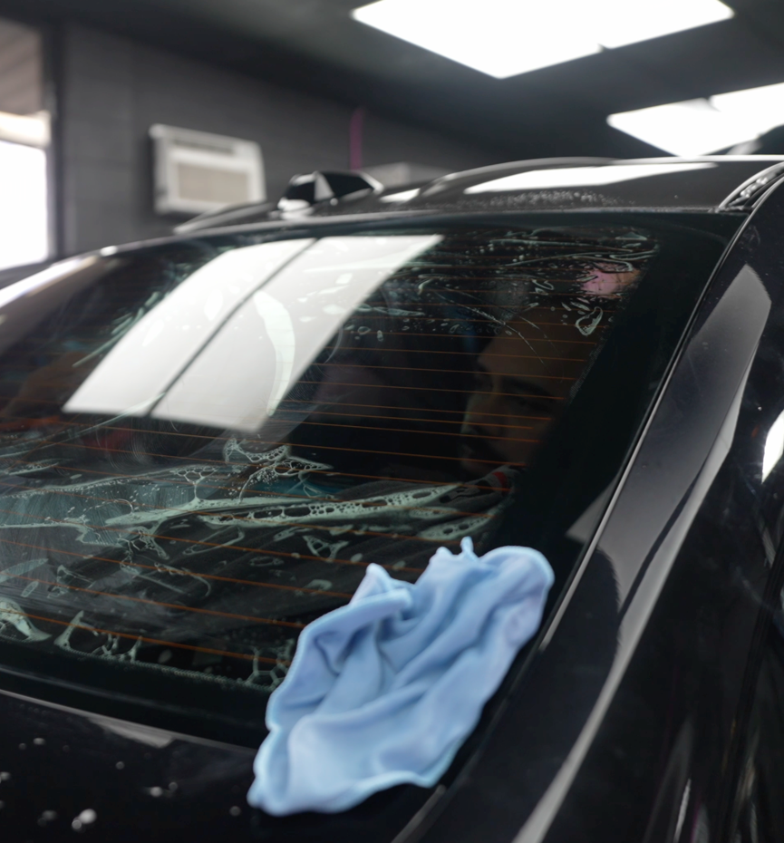 A man is cleaning a white car with a blue cloth.