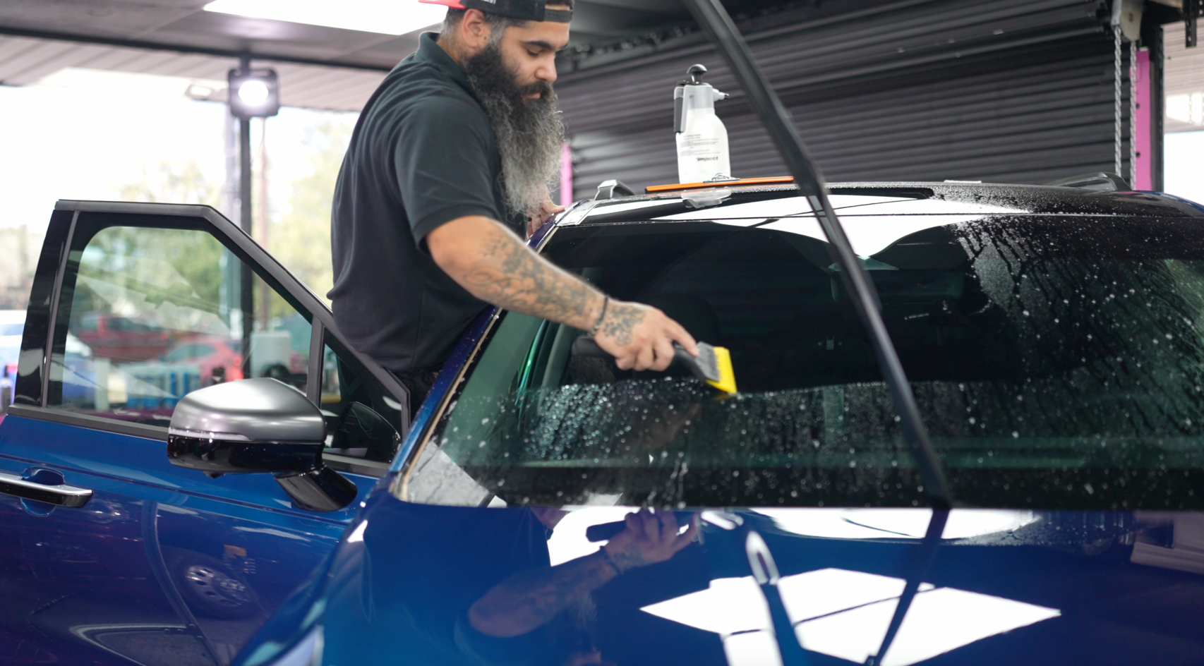 A man with a beard is cleaning the windshield of a blue car.