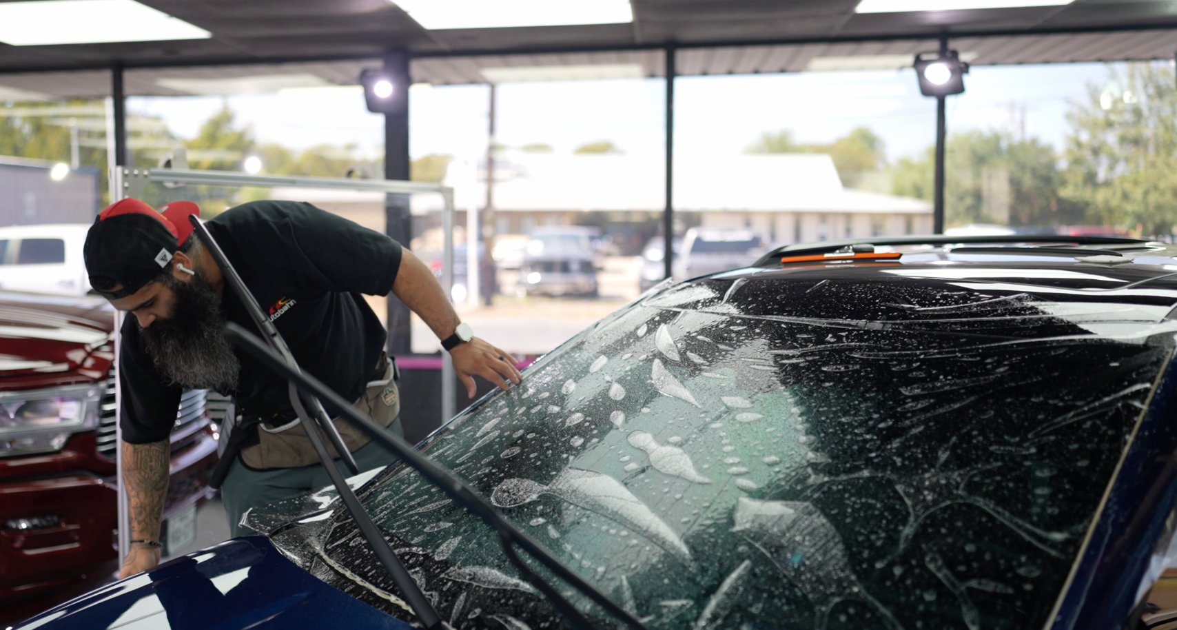 A man is cleaning the windshield of a car in a garage.