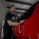A man is working on a red car in a garage.