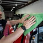 A man is cleaning a car with a green towel.