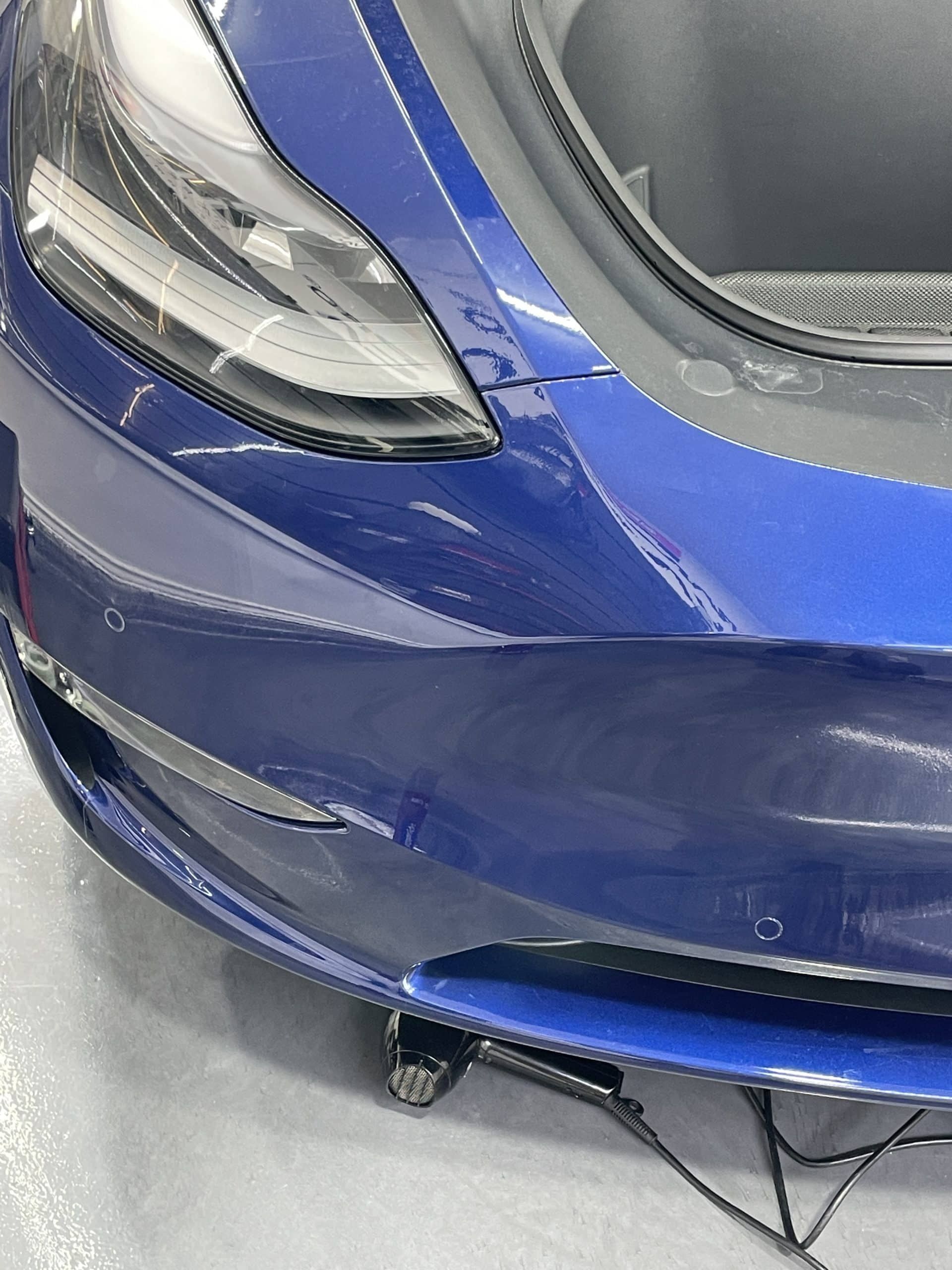 A blue tesla model 3 is parked in a garage