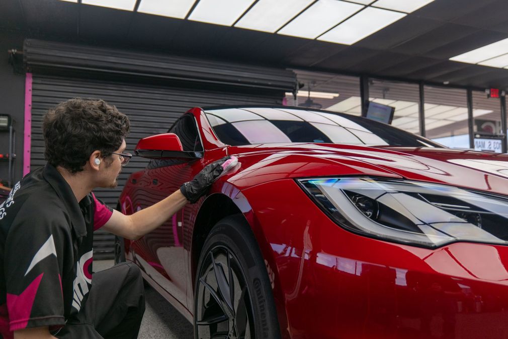 A person in black gloves polishes a red car in a car detailing shop.