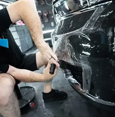 A man is covering the front of a black car with plastic.