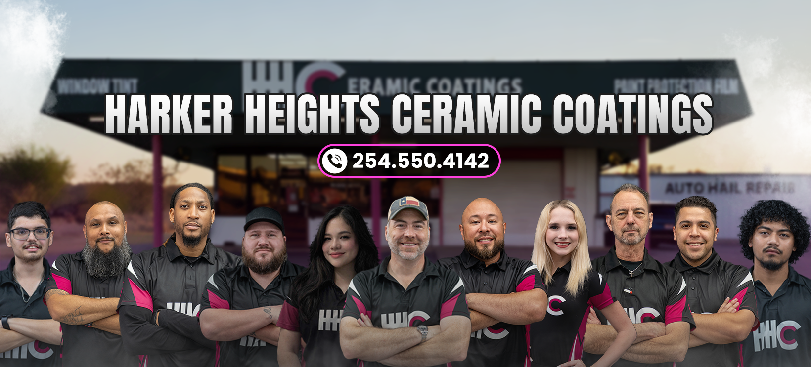 Group of seven people wearing matching black shirts with pink accents, standing in front of a dark wall.