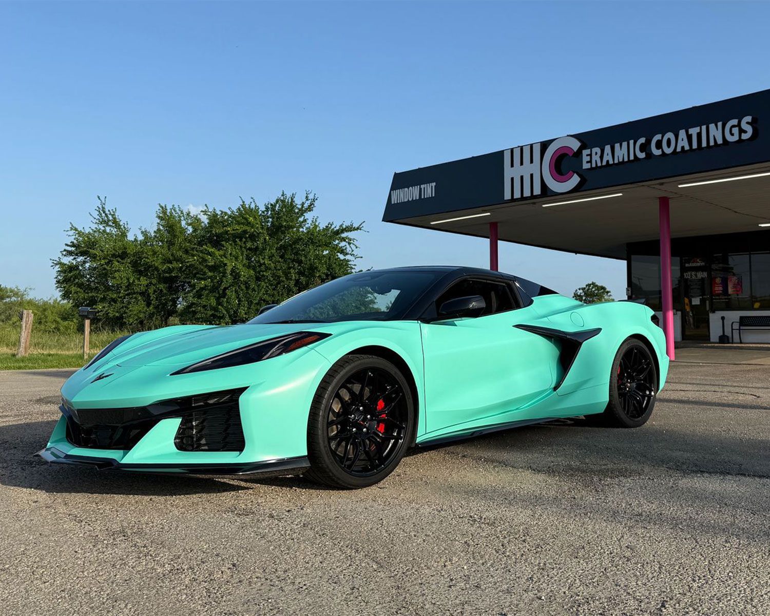 A green sports car is parked in front of a ceramic coatings store.