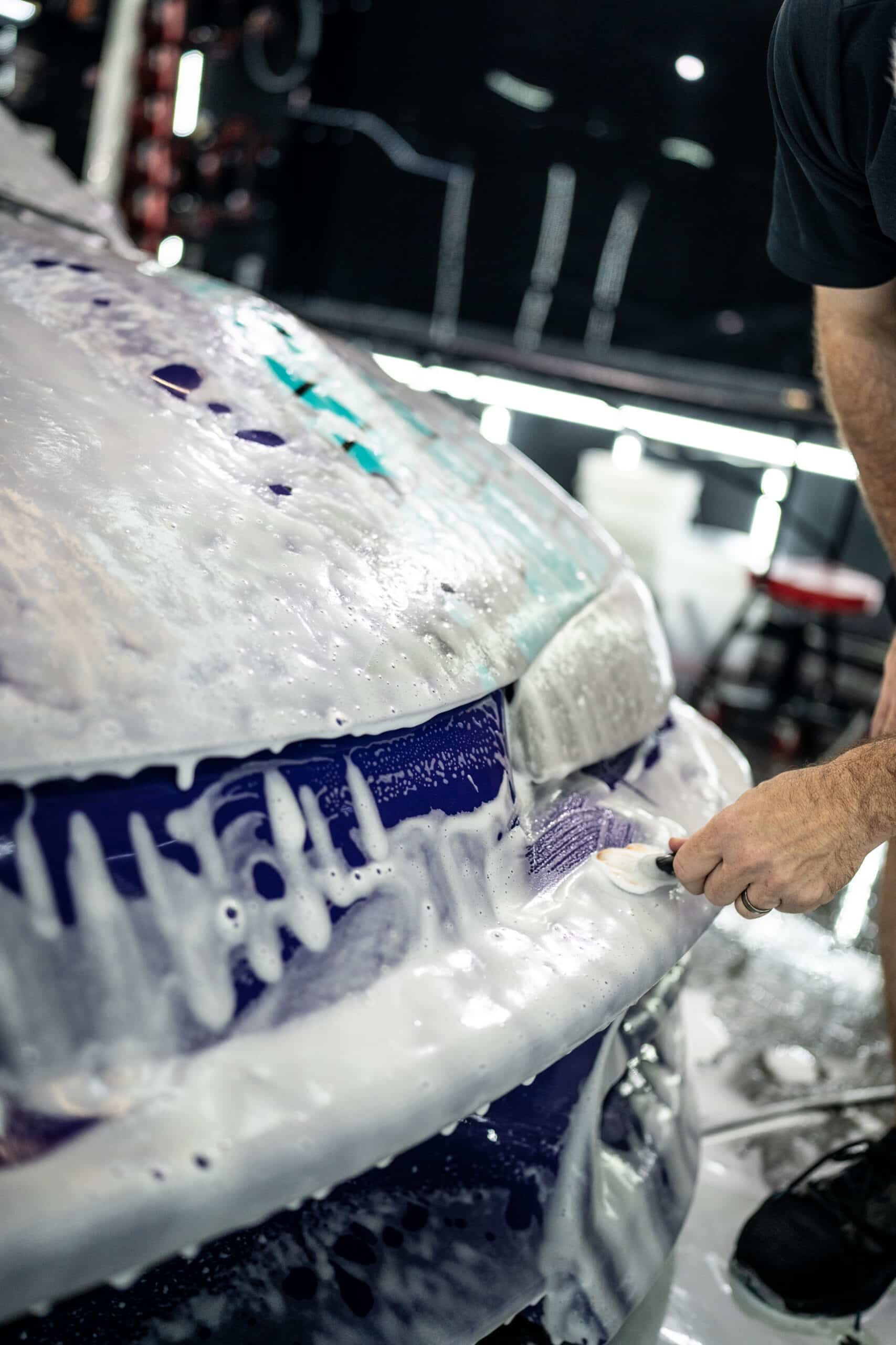 A man is washing a purple car with foam.