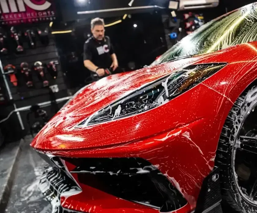 A man is washing a red sports car in a garage.