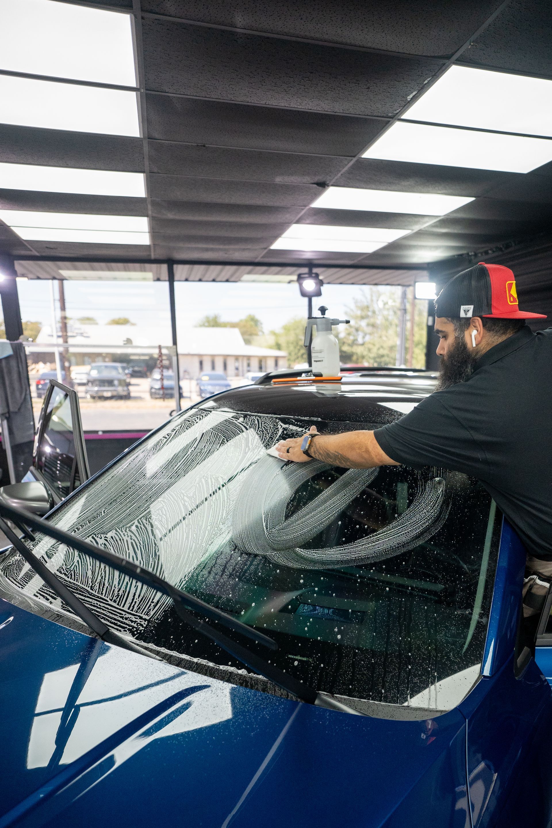 A man is cleaning the windshield of a blue car in a garage.