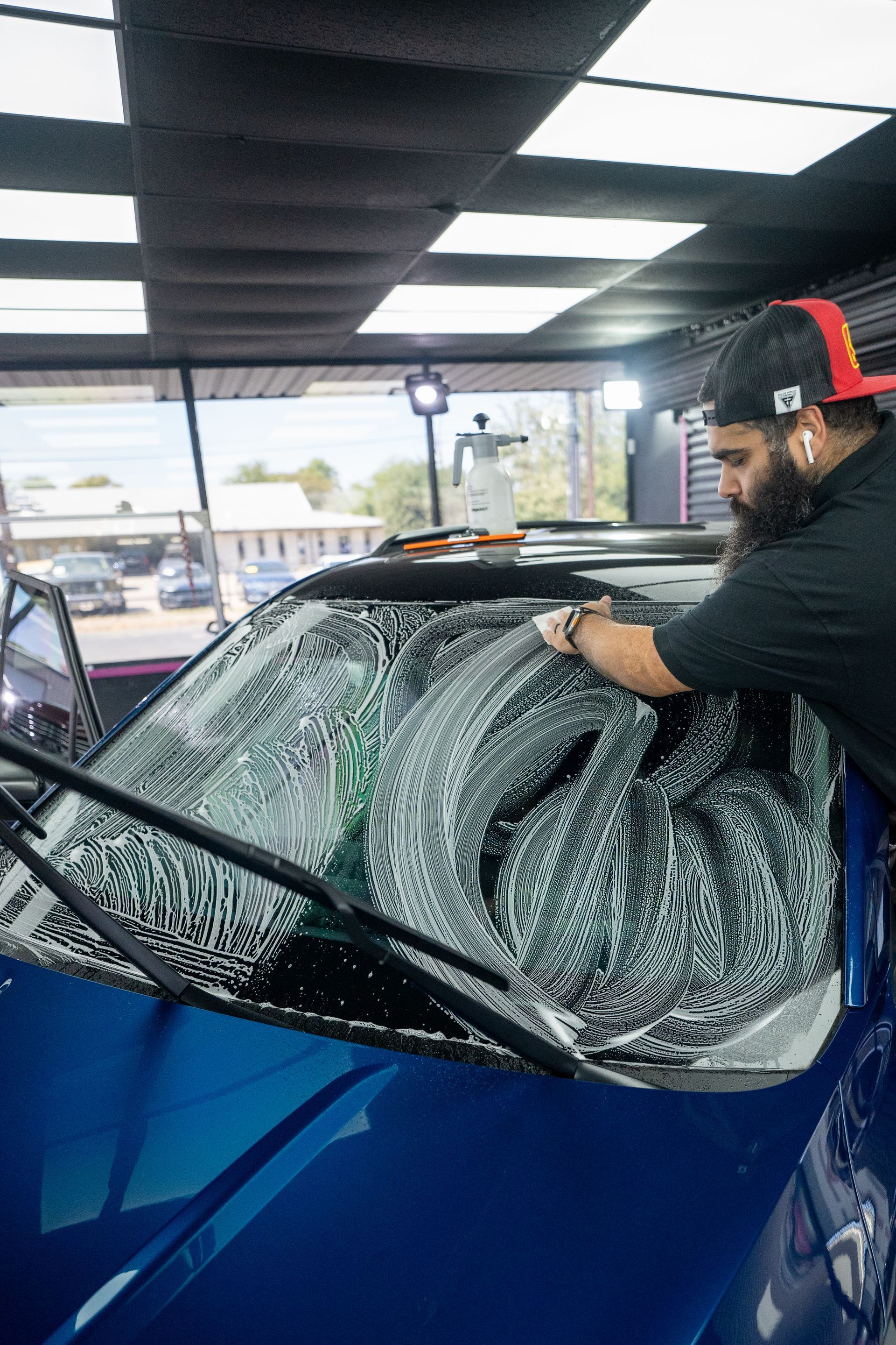 A man is cleaning the windshield of a blue car.