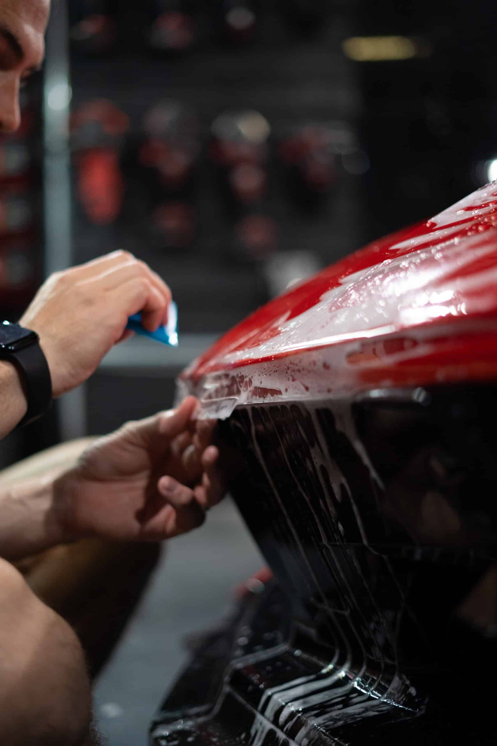 A man is wrapping a red car with a clear film.