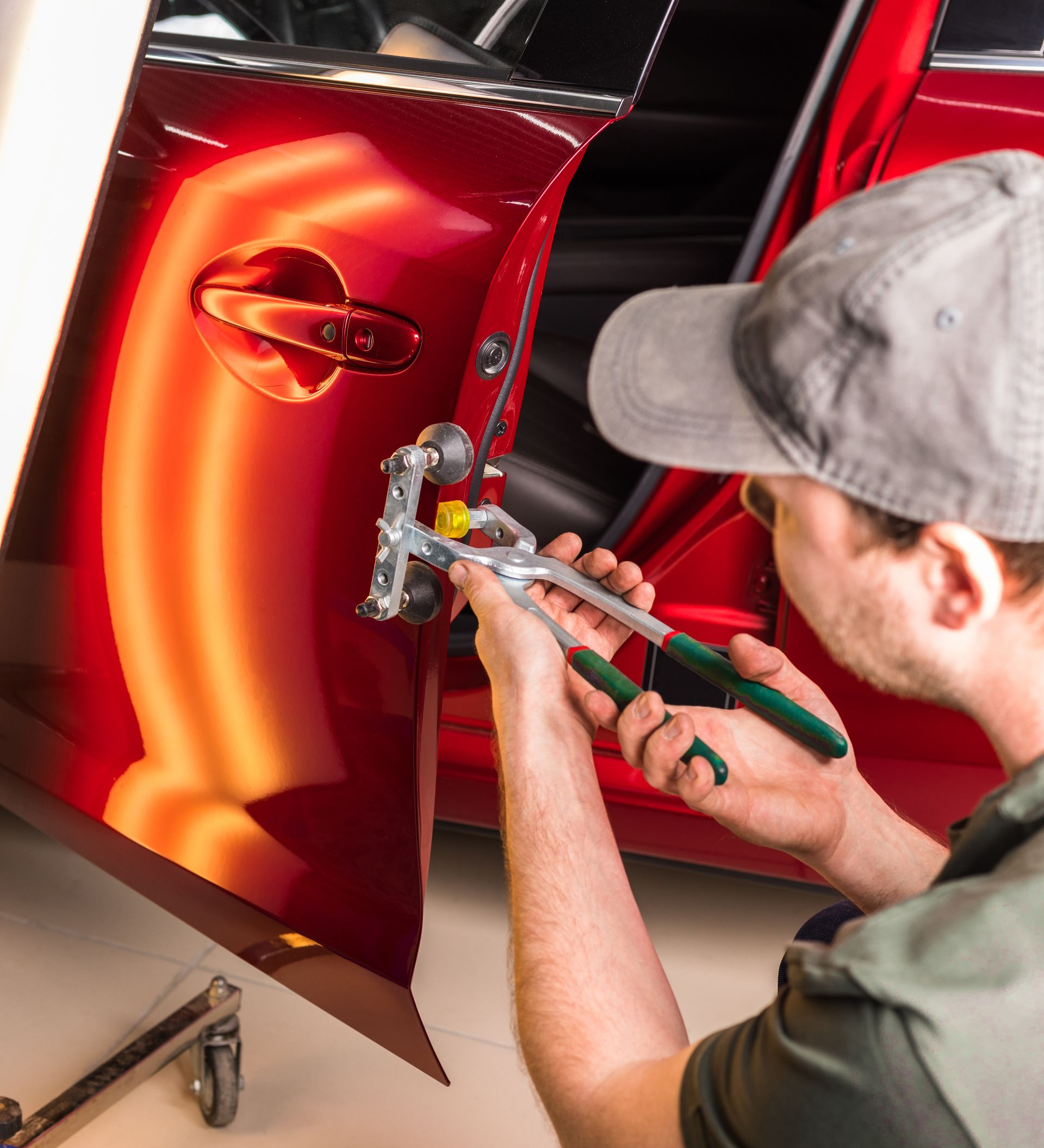 A man is cleaning a red sports car in a garage.