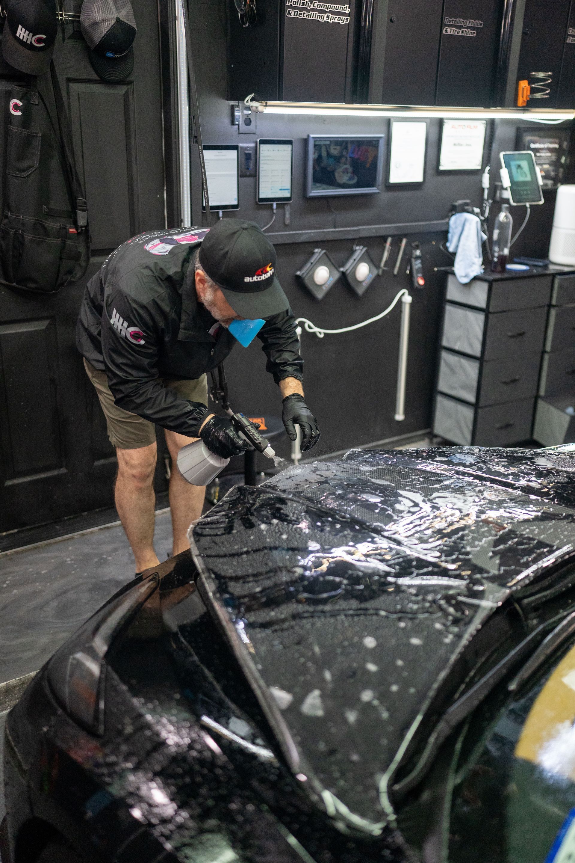 A man is cleaning the hood of a black car in a garage.